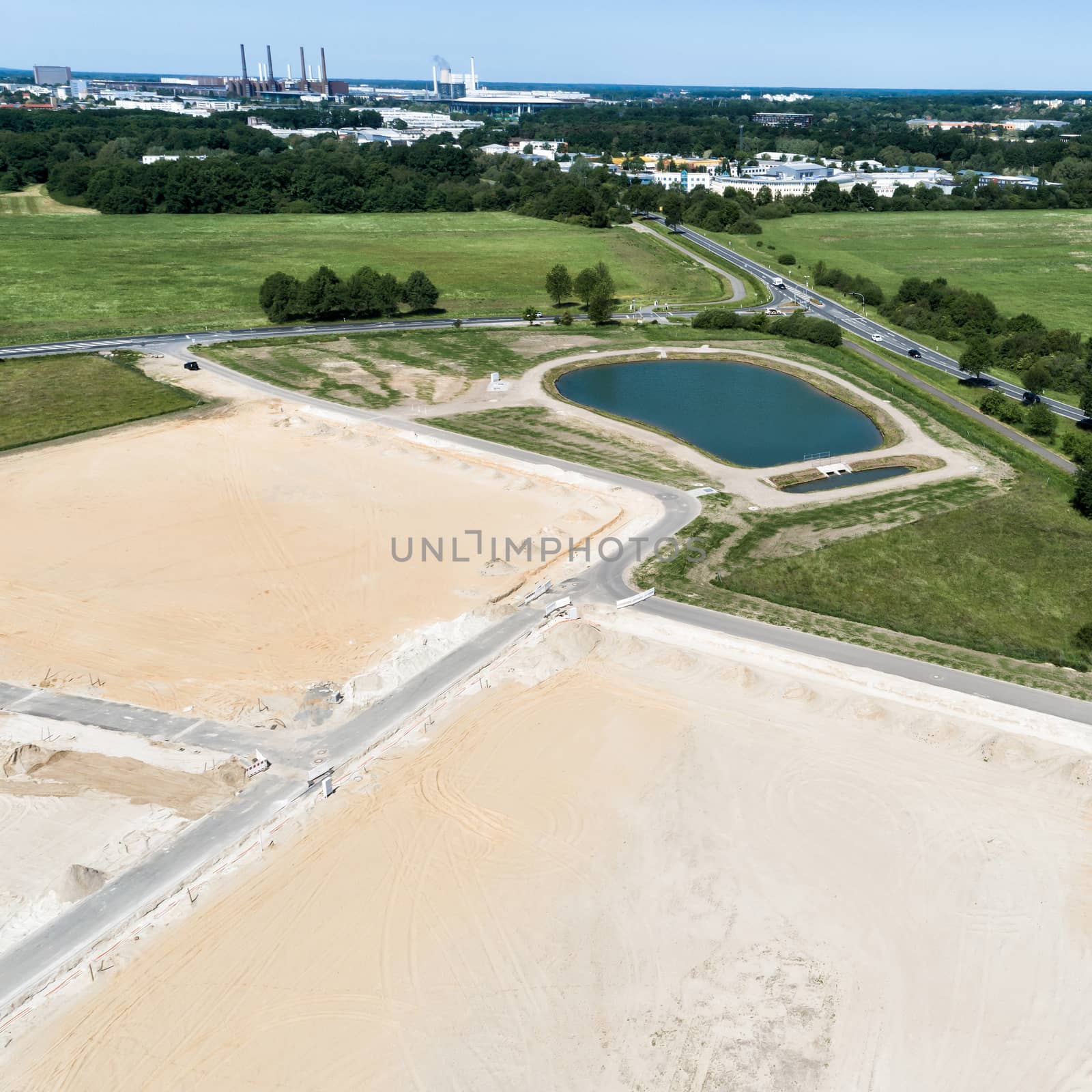Obliquely taken aerial view of a construction site for a new development with a large filled rain retention basin, near Wolfsburg