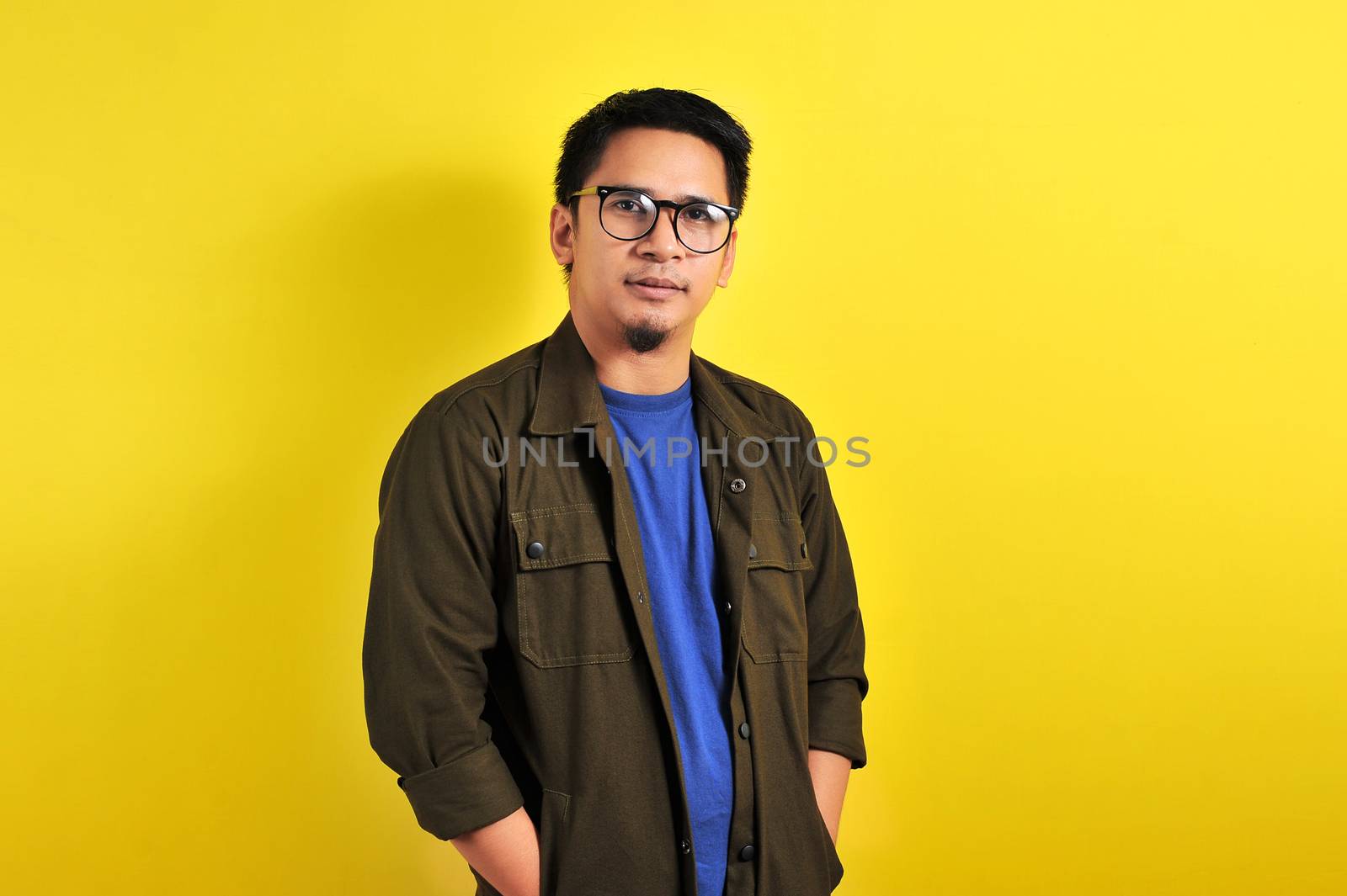 Portrait of confidence young Asian manput his hand in a jacket pocket, isolated on yellow background