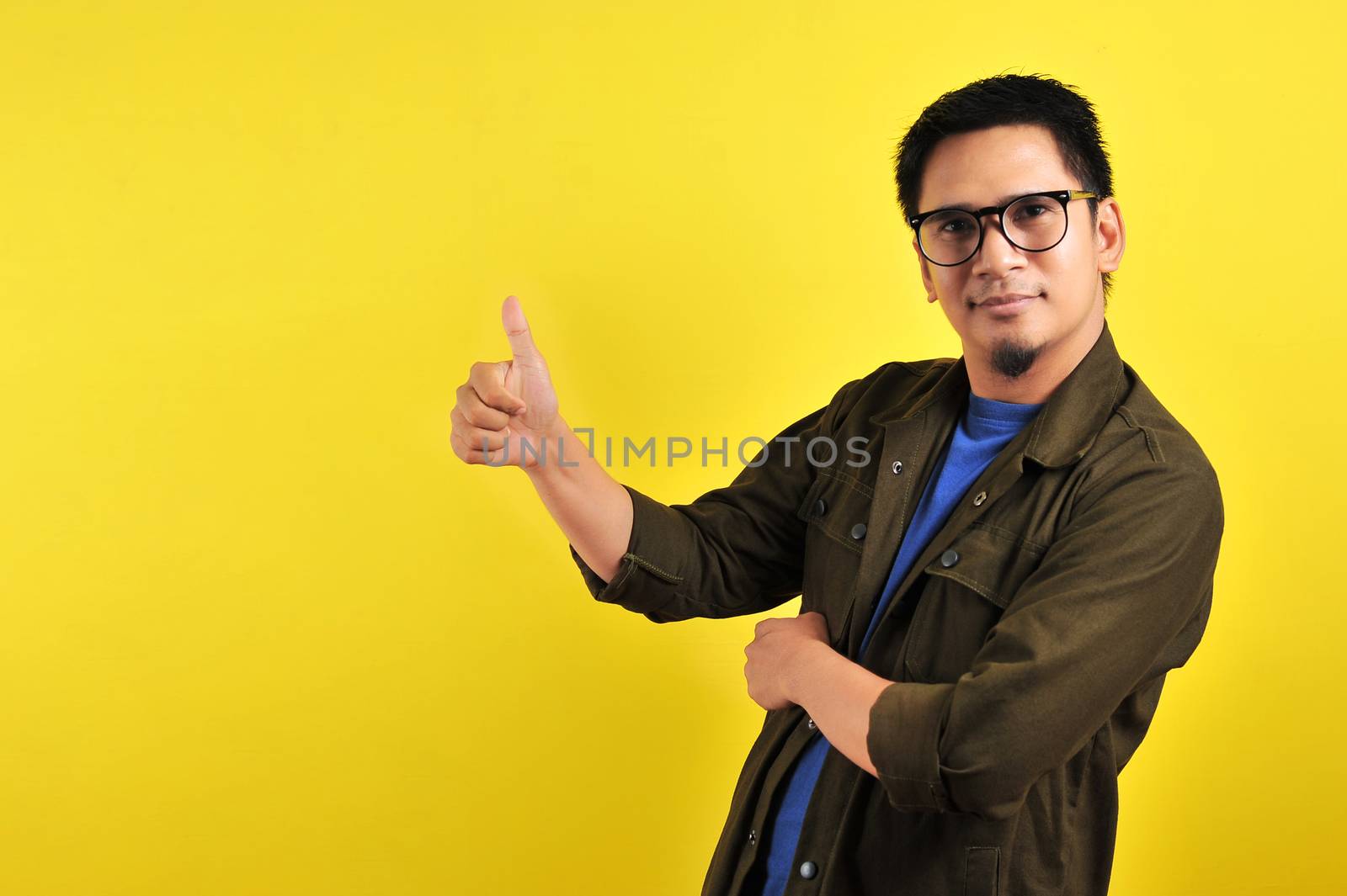 Happy of young Asian man giving thumbs up, copy space, isolated on yellow background