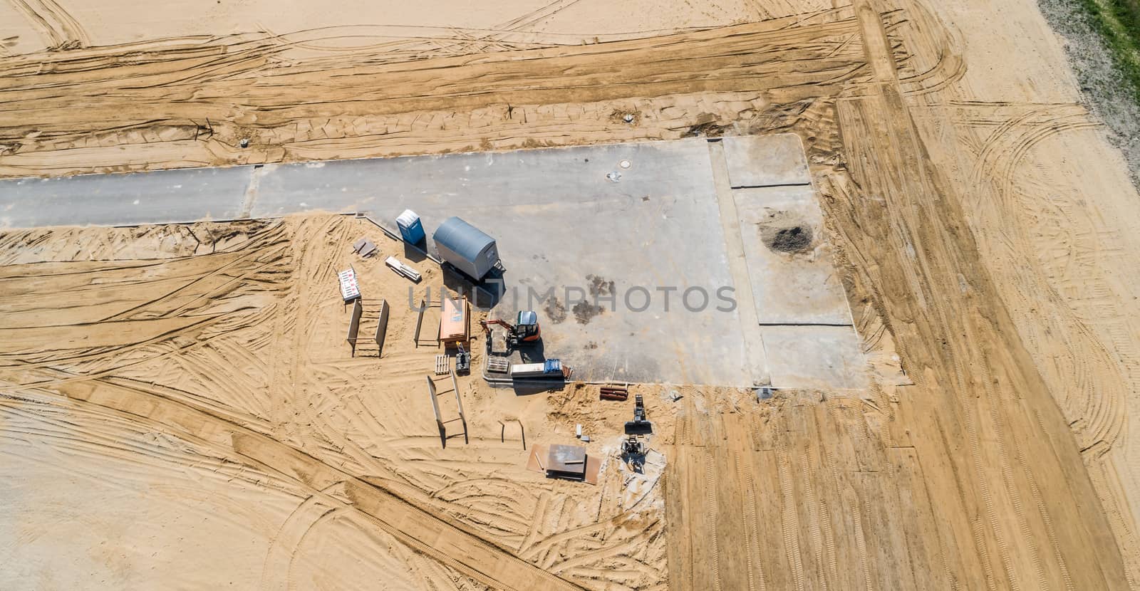 Completed dead-end street in a new development area, as interim storage for construction machinery, building materials and a construction wagon with mobile toilet, inclined aerial view by geogif