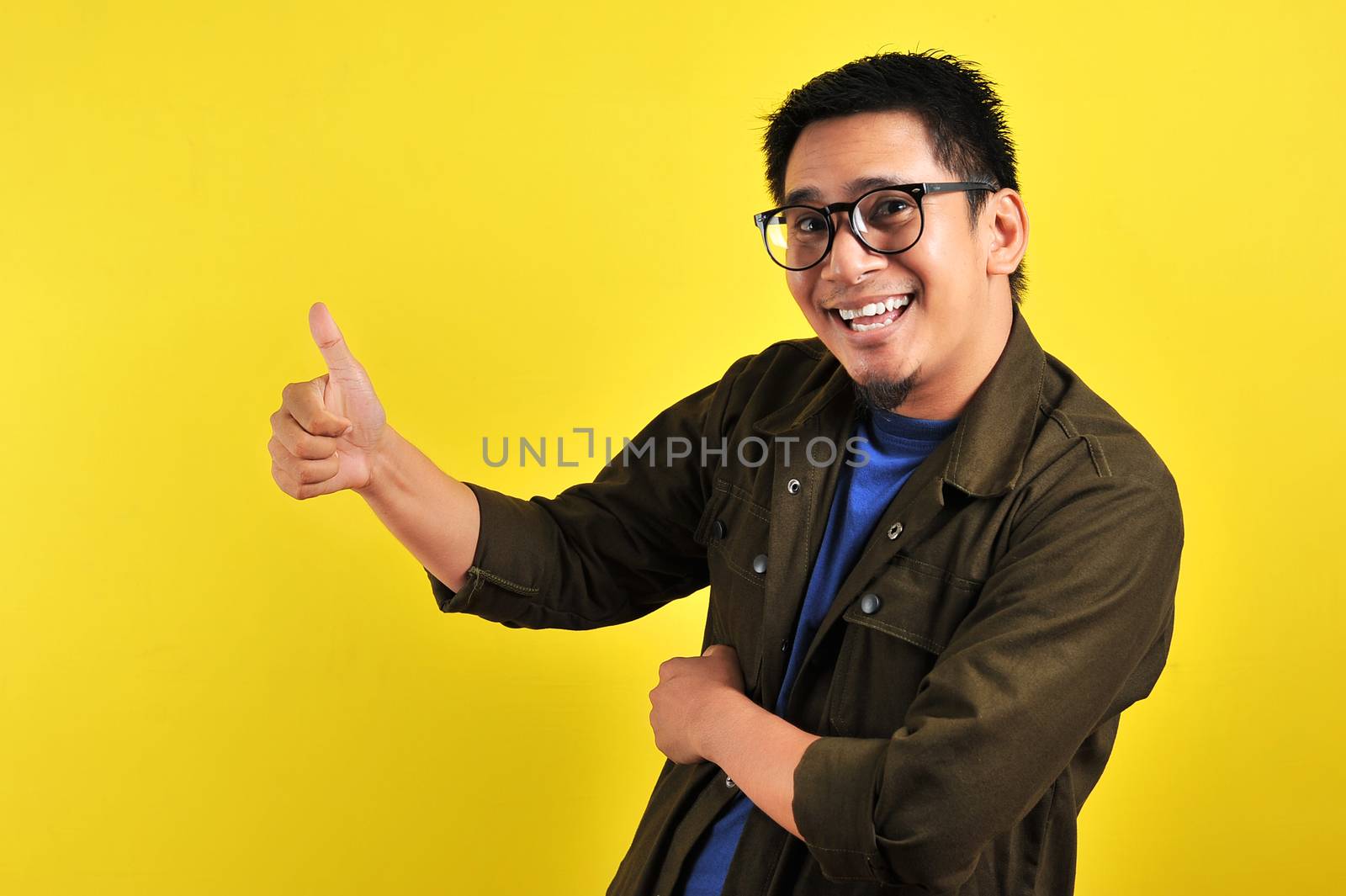 Happy of young Asian man smiling and giving thumbs up, copy space, isolated on yellow background