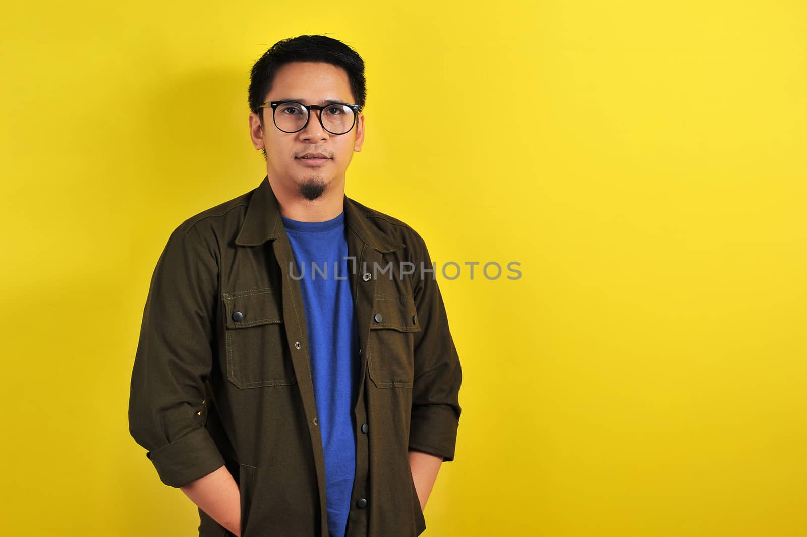 Portrait of confidence young Asian manput his hand in a jacket pocket, isolated on yellow background