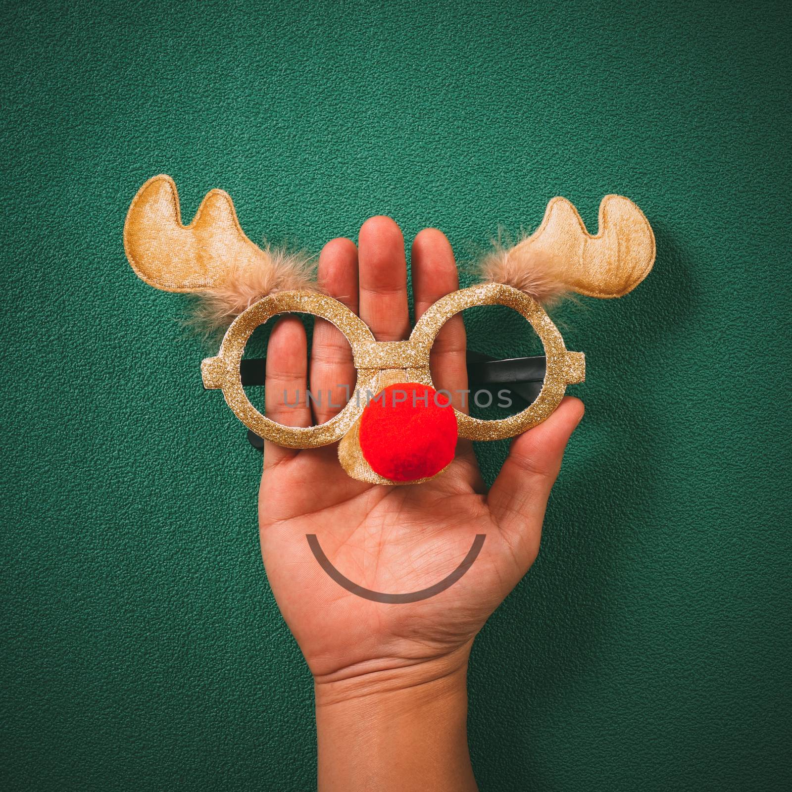 Christmas glasses that decoration with Christmas reindeer and red ball on hand on green  background