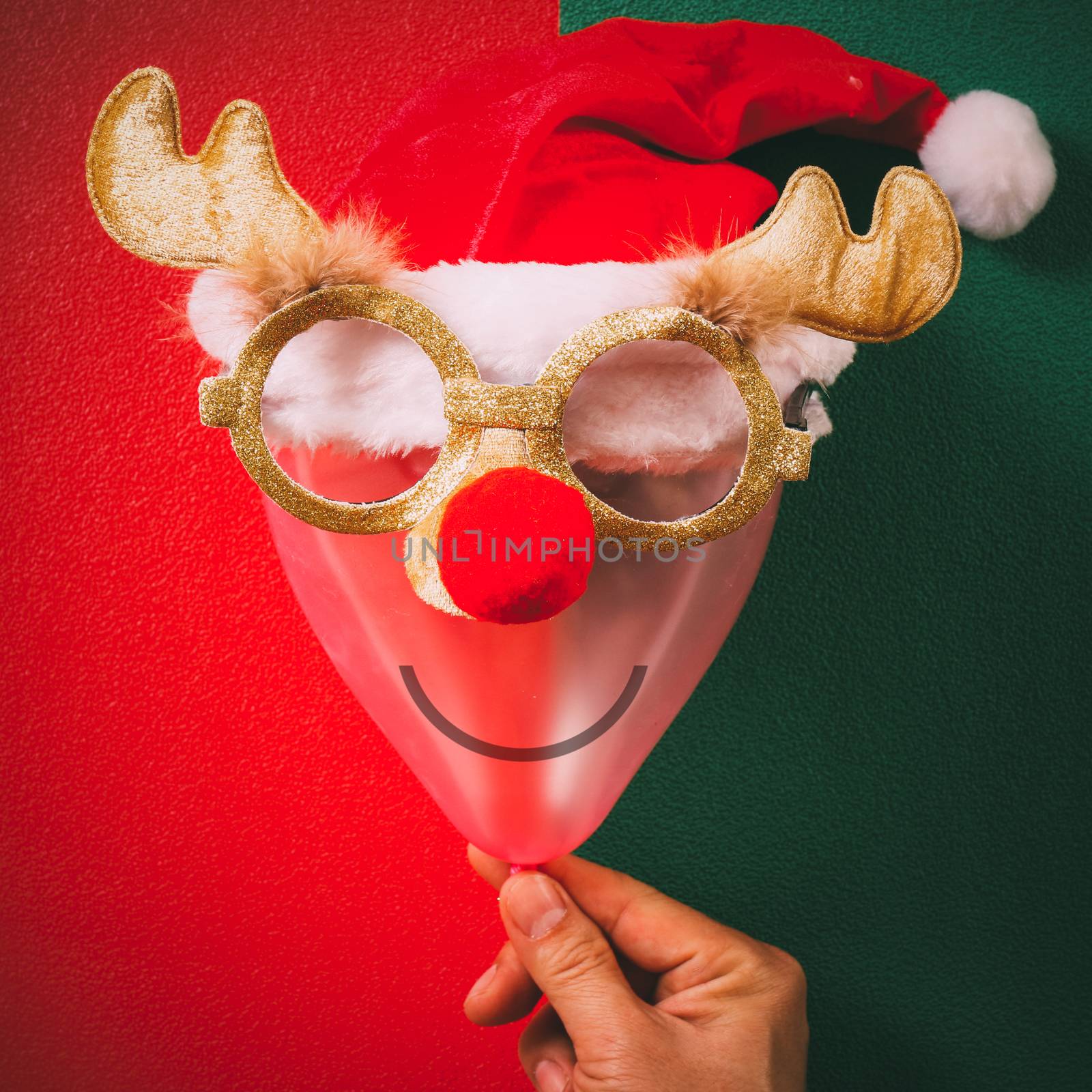 Hand holding Christmas glasses that decoration with reindeer and red hat on air bolloon on green and red background