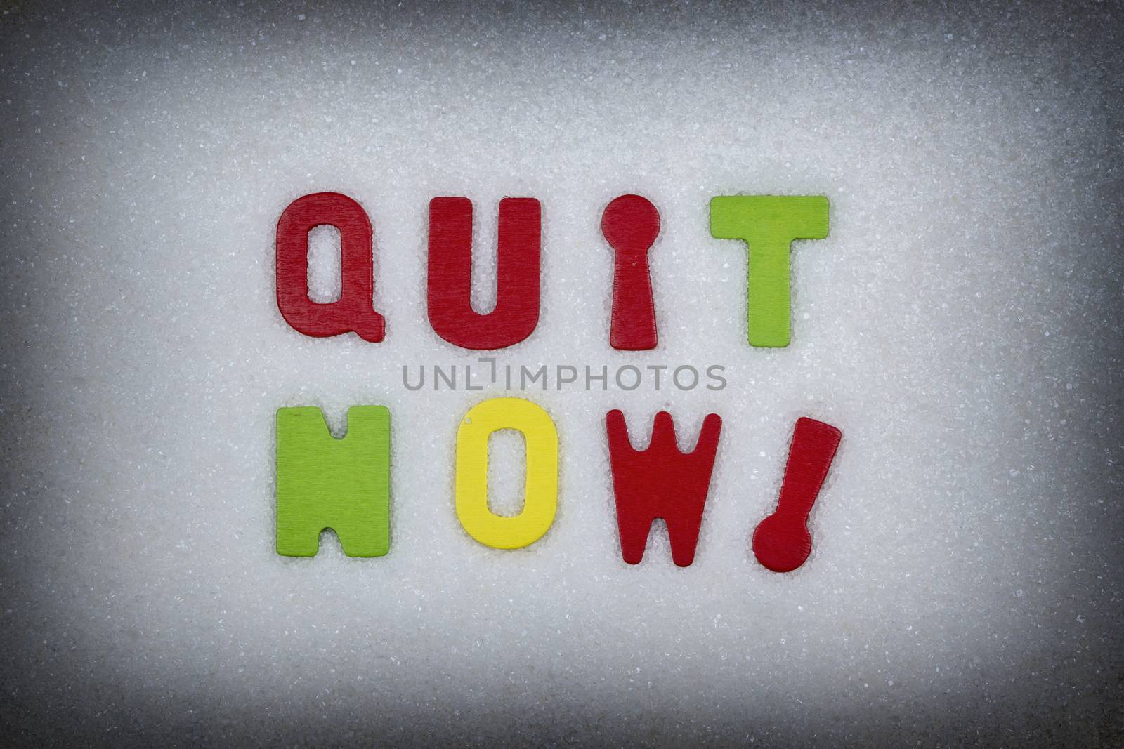 "Quit now!" Colorful text and letters in wood on white sugar crystals background and black vignette border