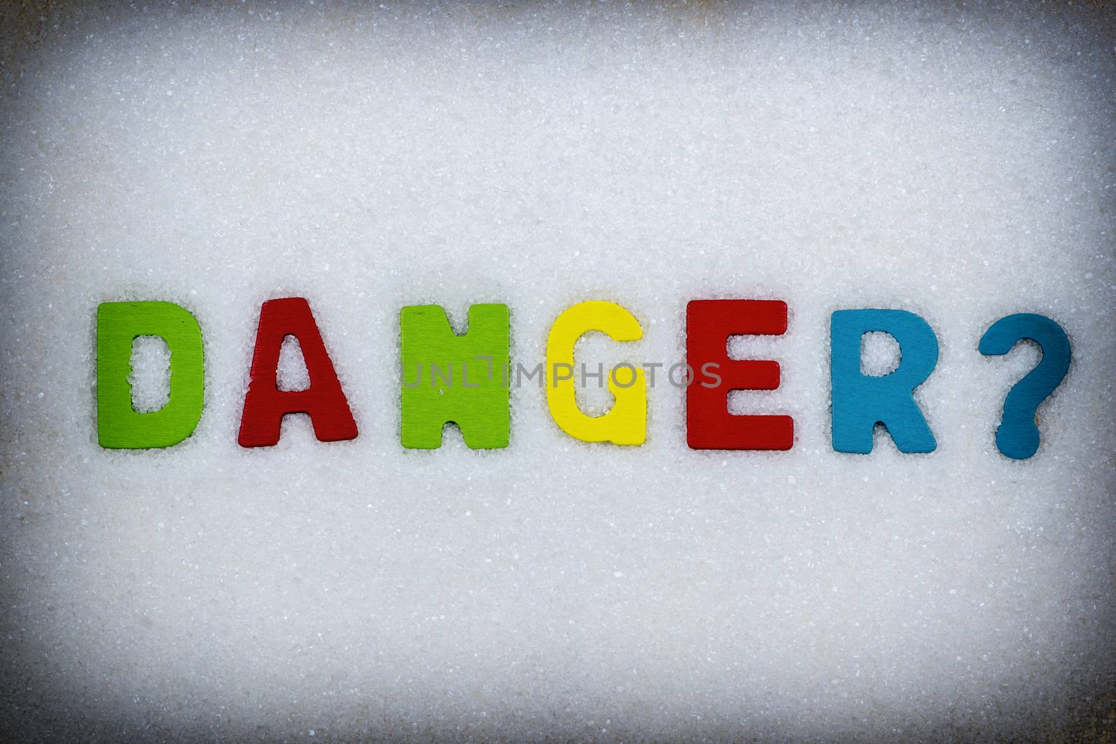 "Danger?" Colorful text and letters in wood on white sugar crystals background and black vignette border