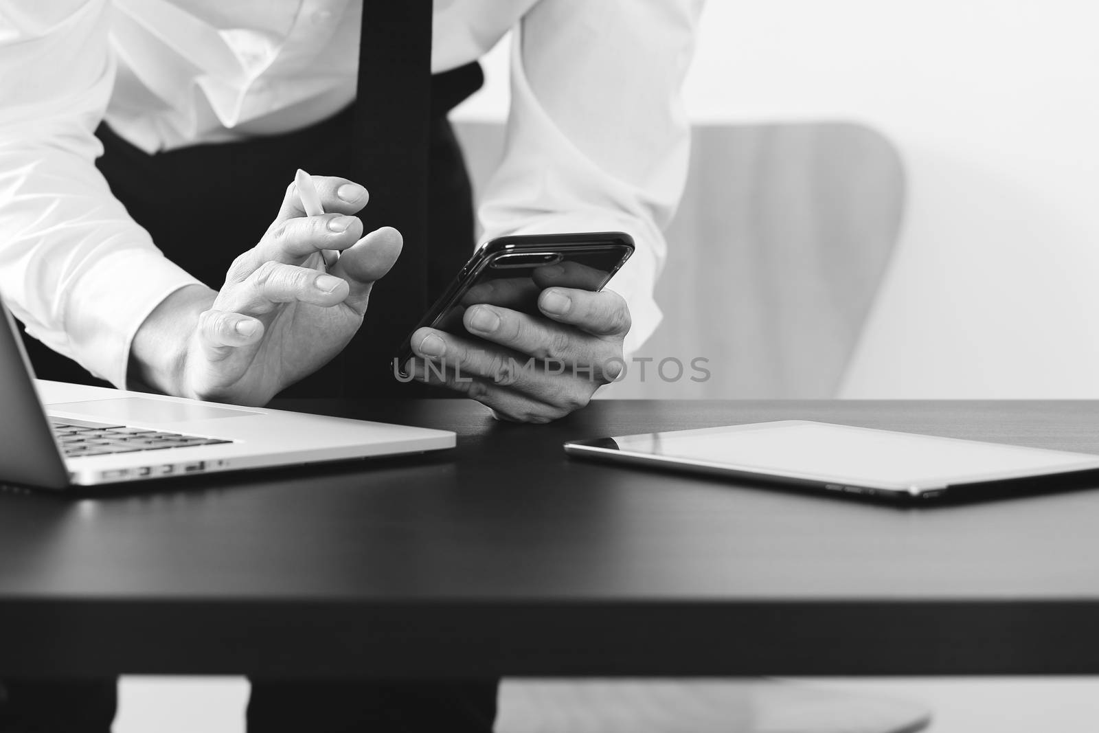 close up of businessman working with smart phone and digital tablet and laptop computer on wooden desk in modern office ,black and white