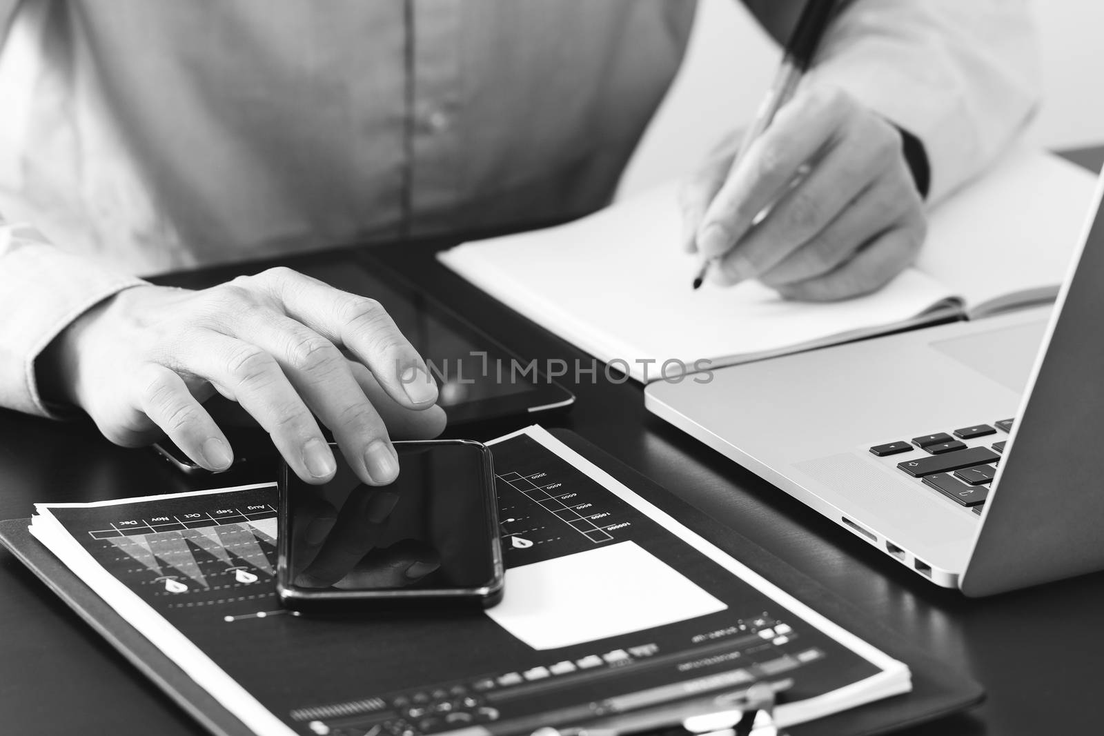 close up of businessman working with smart phone and digital tablet and laptop computer  on wooden desk in modern office,black and white