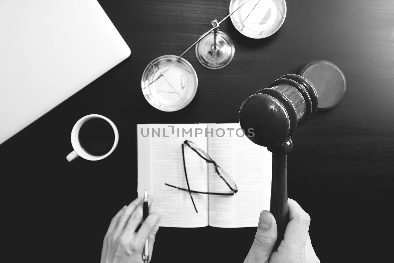 justice and law concept.Top view of Male judge hand in a courtroom with the gavel and brass scale and computer and open bible book on dark wood table,black and white