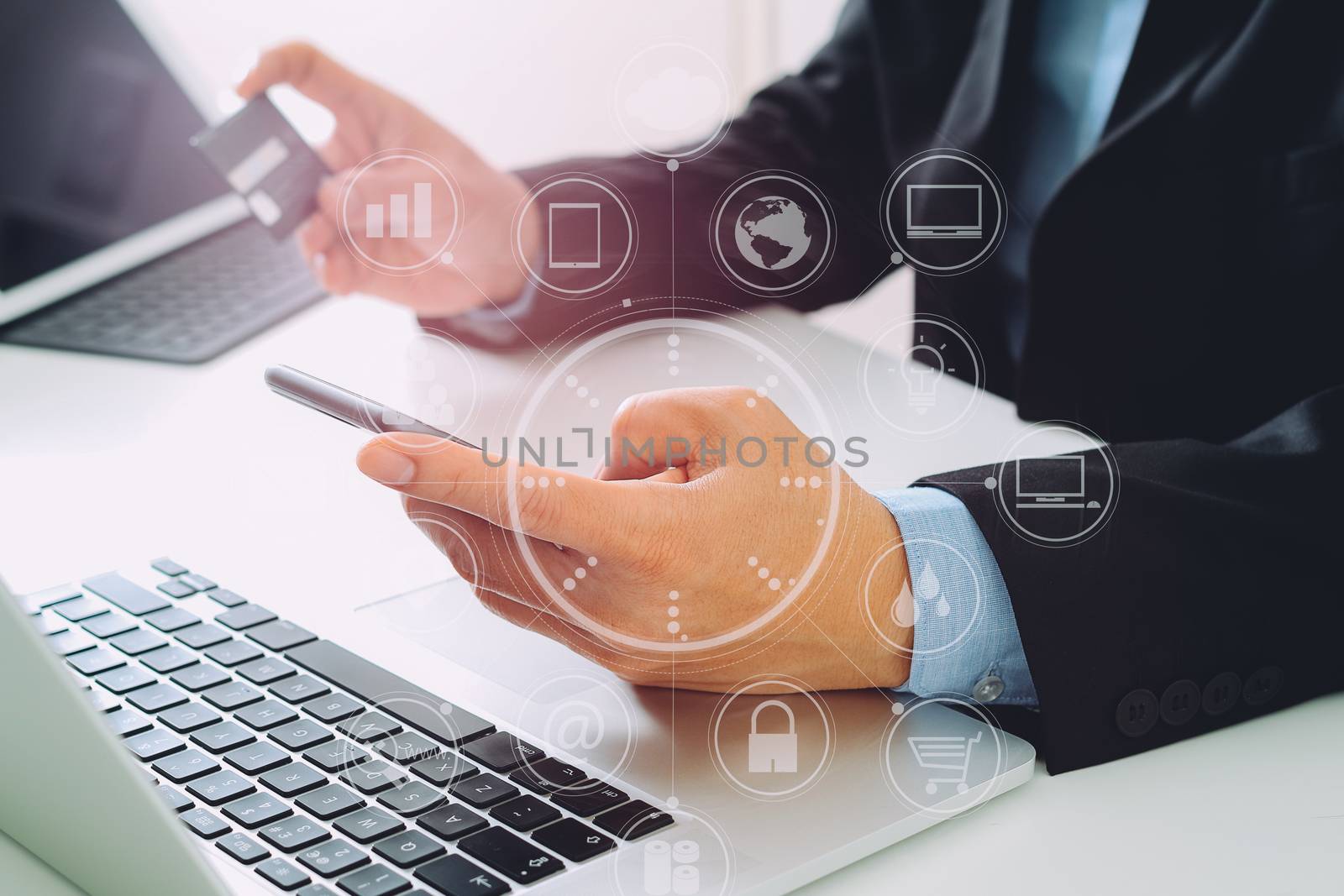 businessman making credit card purchase online with mobile phone and laptop computer on modern desk with VR icon diagram