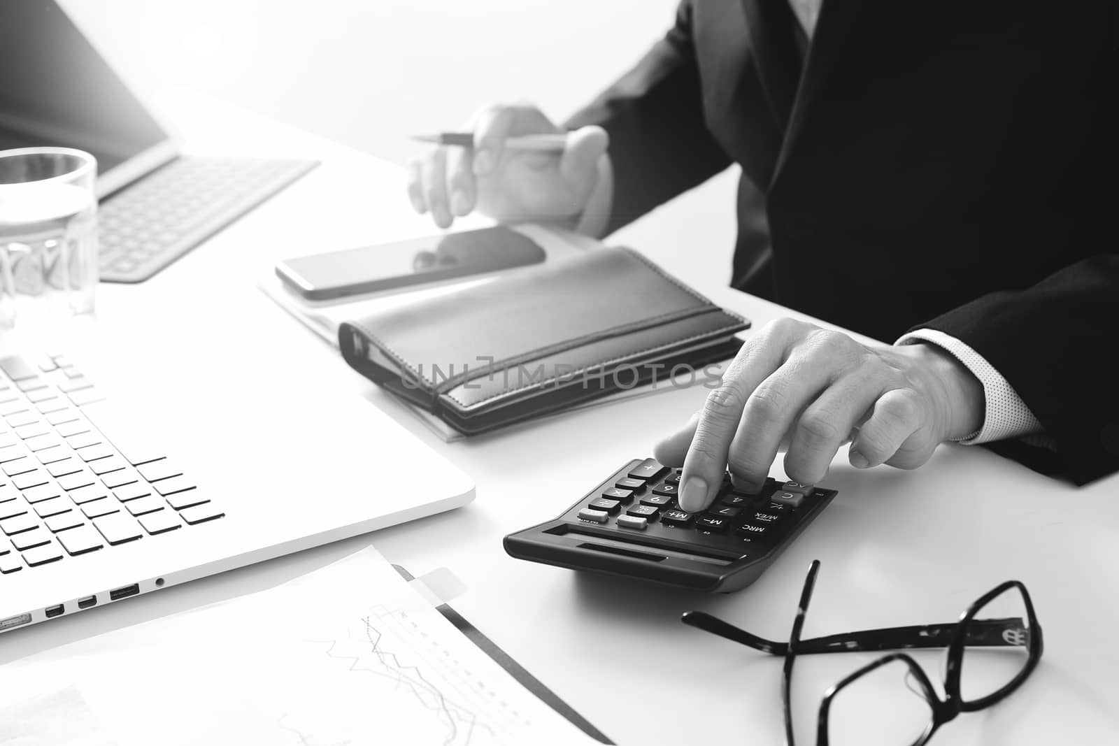 businessman hand working with finances about cost and calculator and latop with mobile phone on withe desk in modern office,black and white