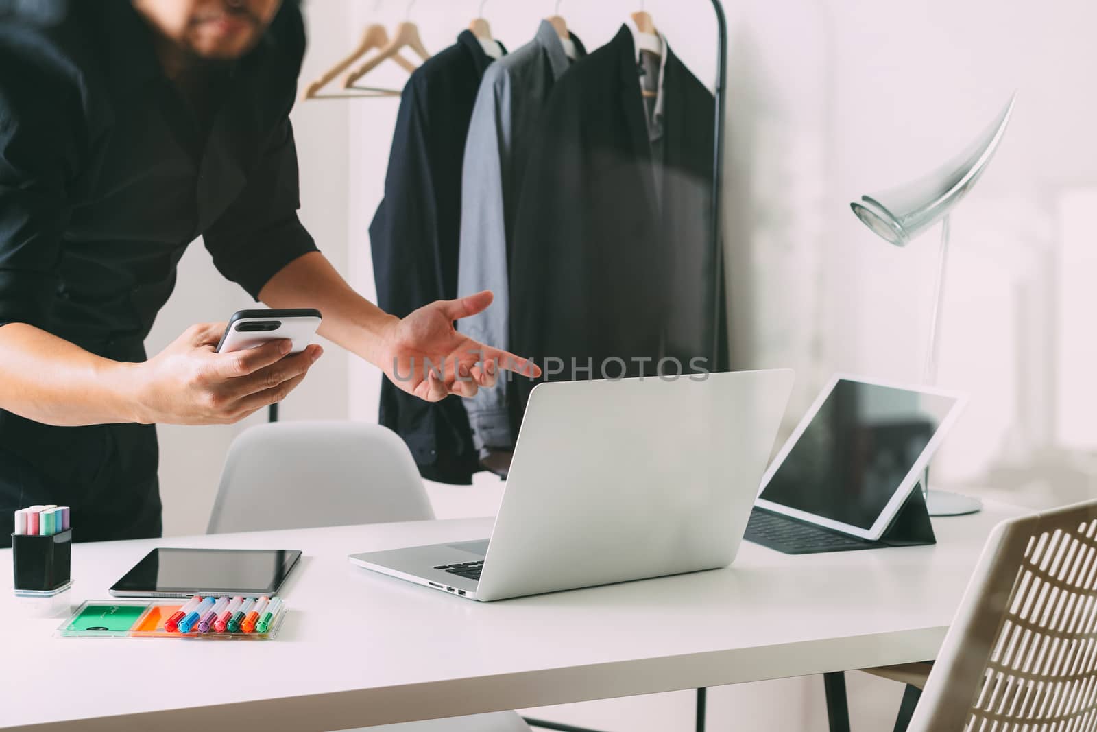 Fashion designer talking mobile phone and using laptop with digital tablet computer in modern studio