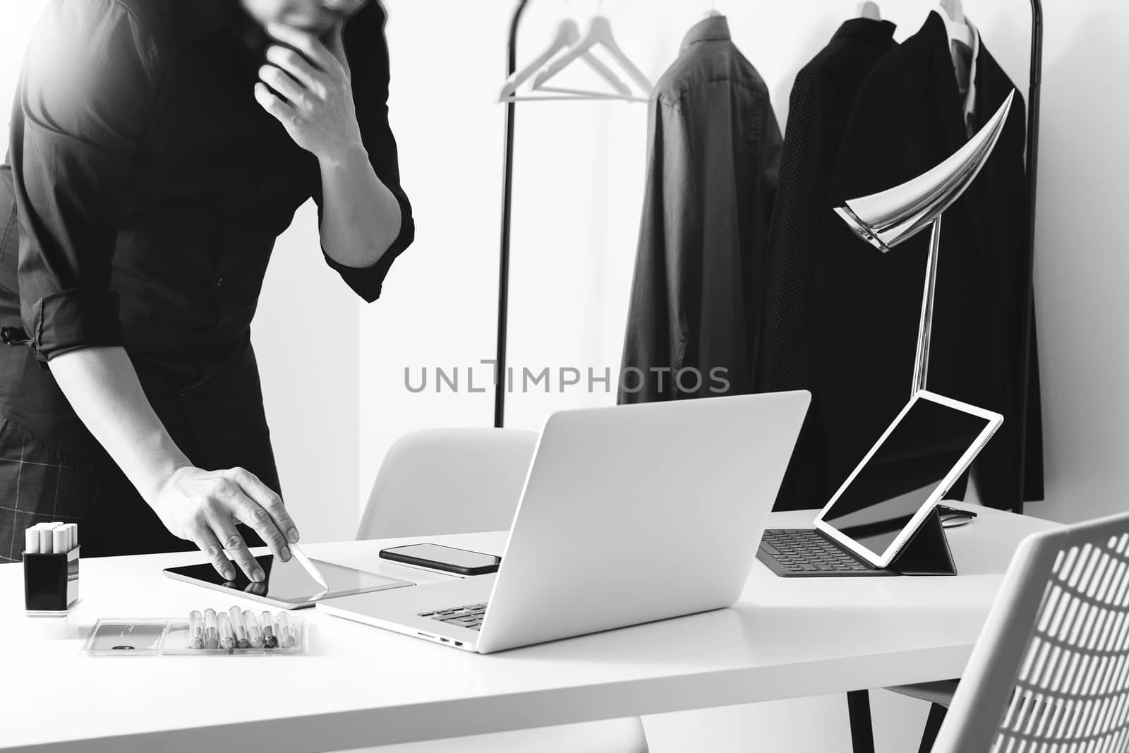 Fashion designer talking mobile phone and using laptop with digital tablet computer in modern studio,black and white
