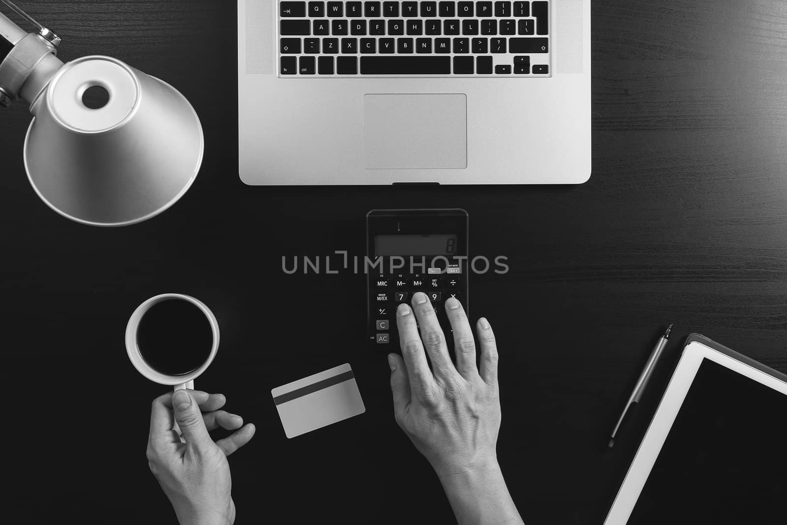 Internet shopping concept.Top view of hands working with calculator and laptop and credit card and tablet computer on dark wooden table background,black and white