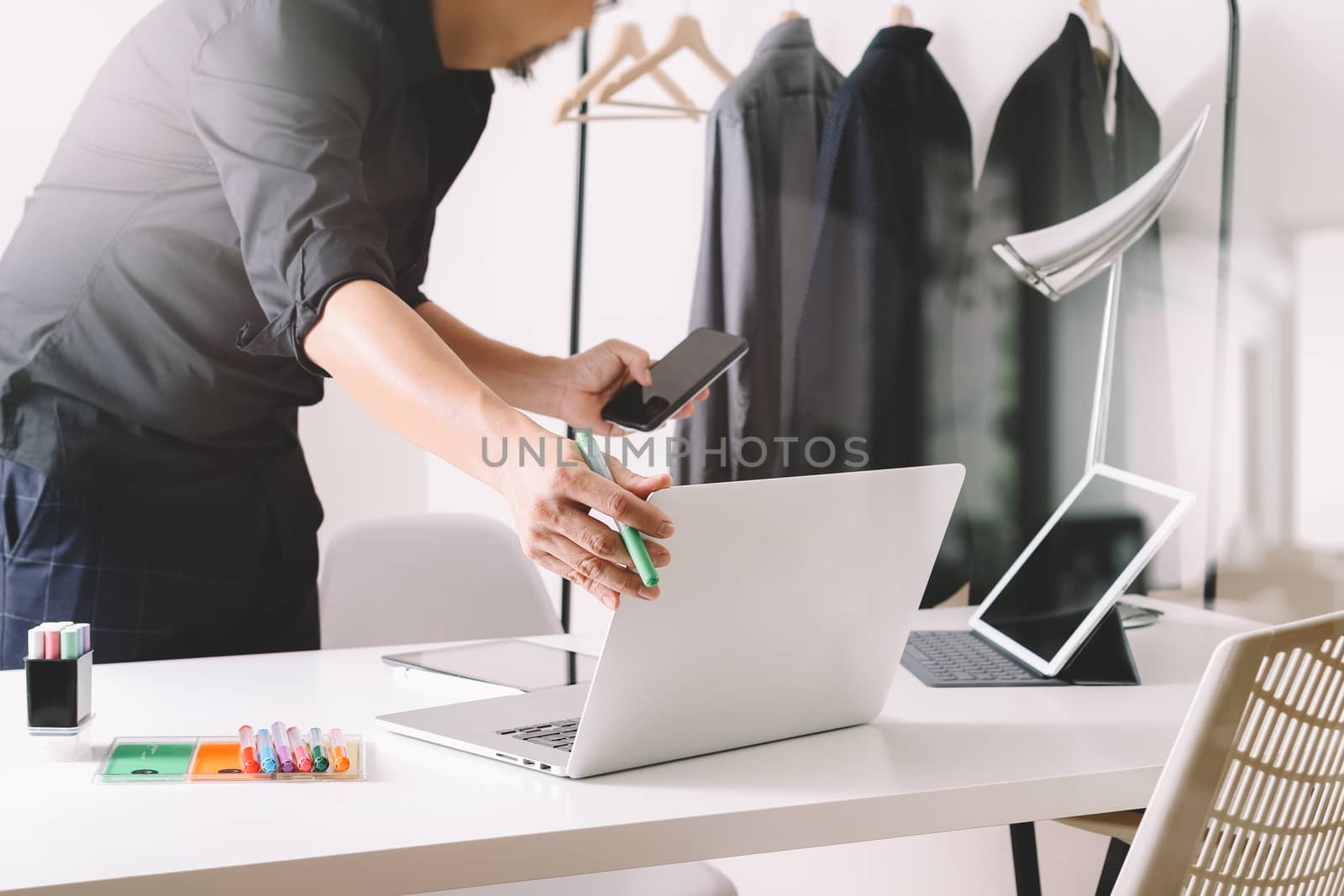 Fashion designer working with mobile phone and using laptop with digital tablet computer in modern studio 