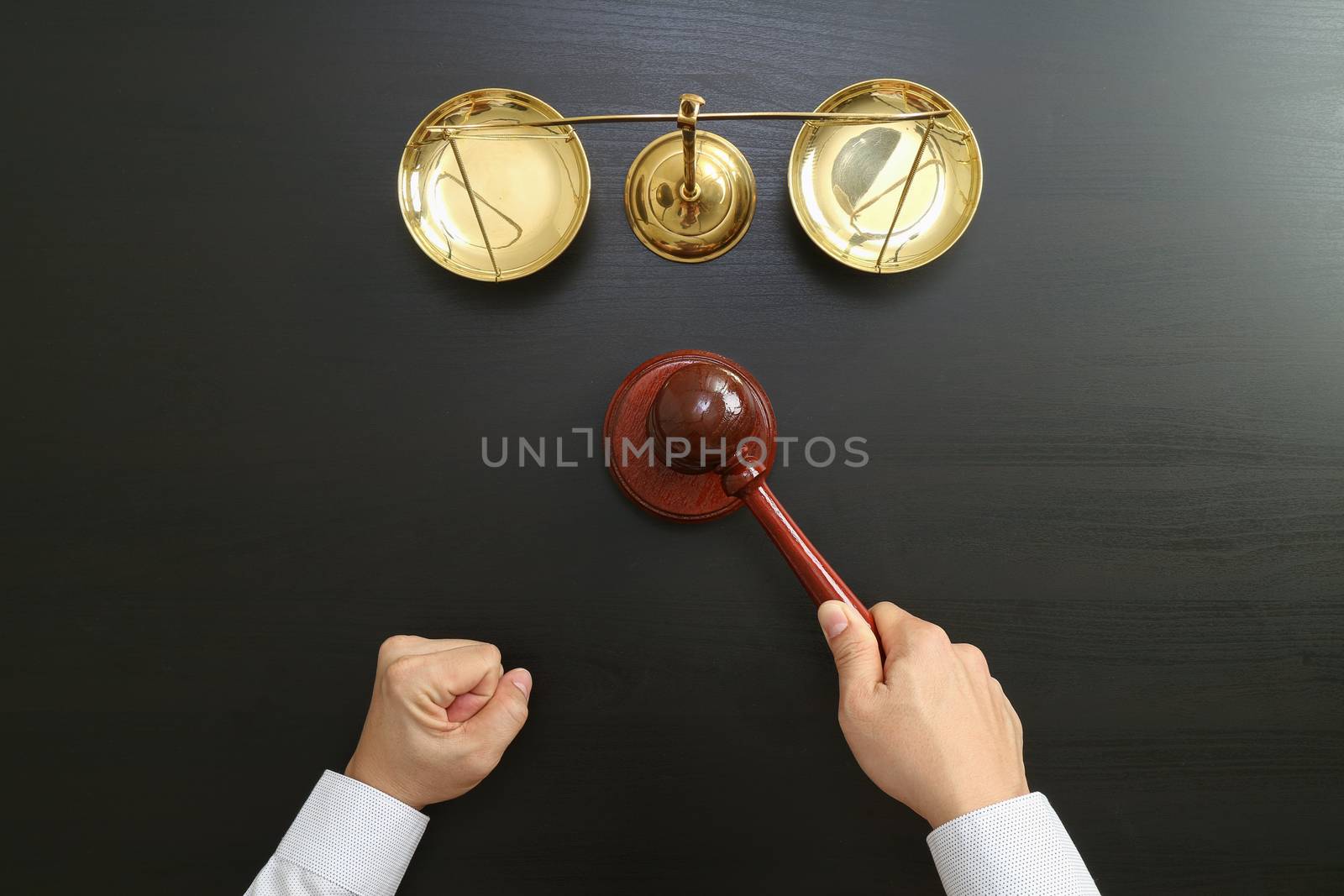 justice and law concept.Top view of Male judge hand in a courtroom with the gavel and brass scale on dark wood table