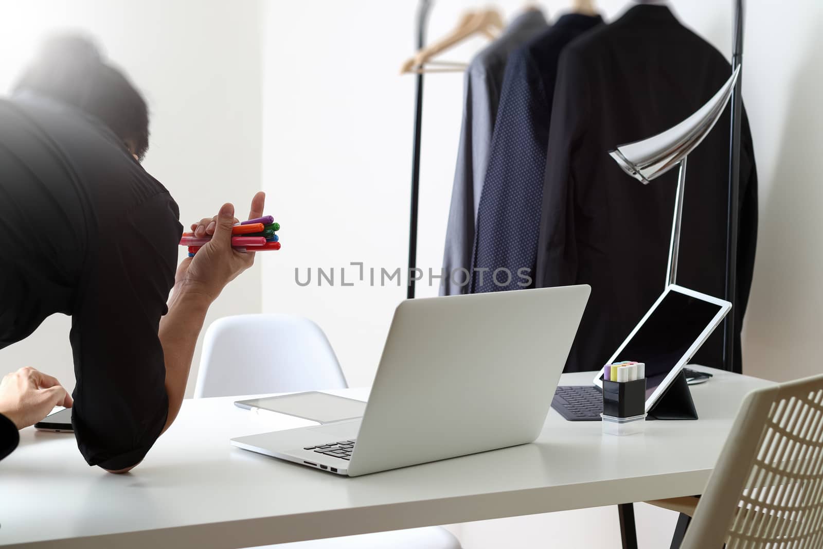 Fashion designer working with mobile phone and using laptop with digital tablet computer in modern studio with city exposure