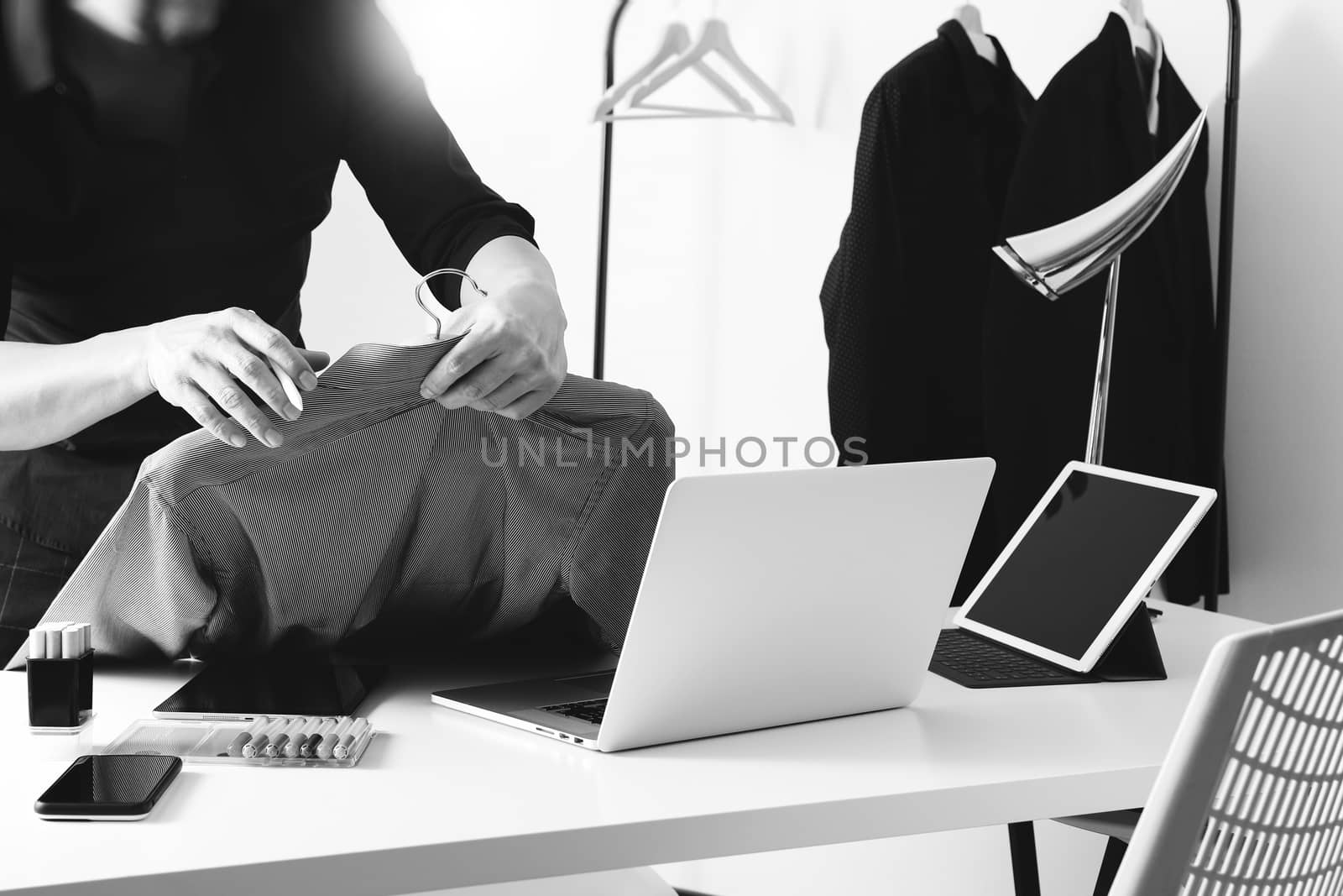 Fashion designer holding shirt and using laptop with digital tablet computer in modern studio ,black and white