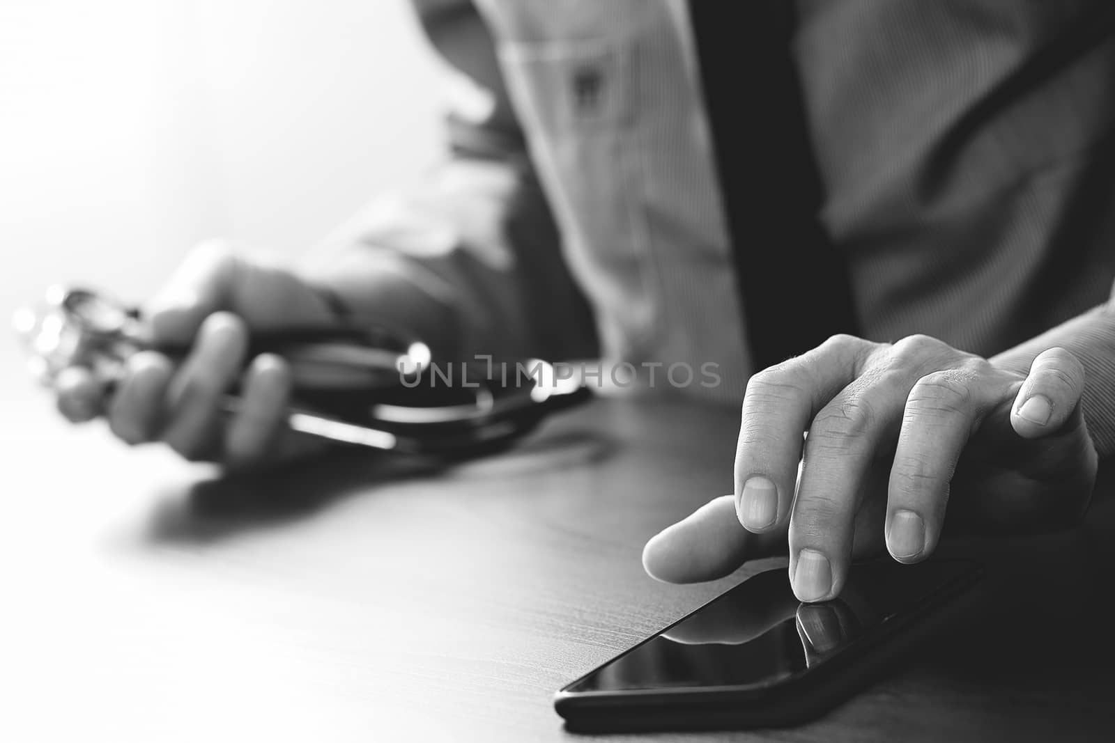 close up of smart medical doctor working with mobile phone and stethoscope on dark wooden desk,black and white  