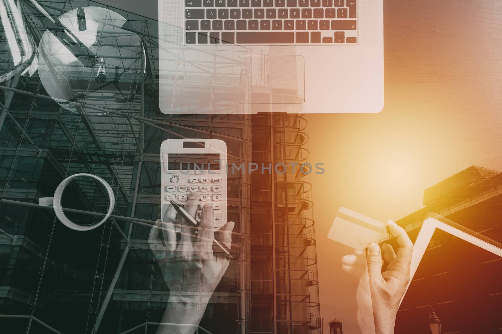 Internet shopping concept.Top view of hands working with calculator and laptop and credit card and tablet computer on dark wooden table background with buildings exposure