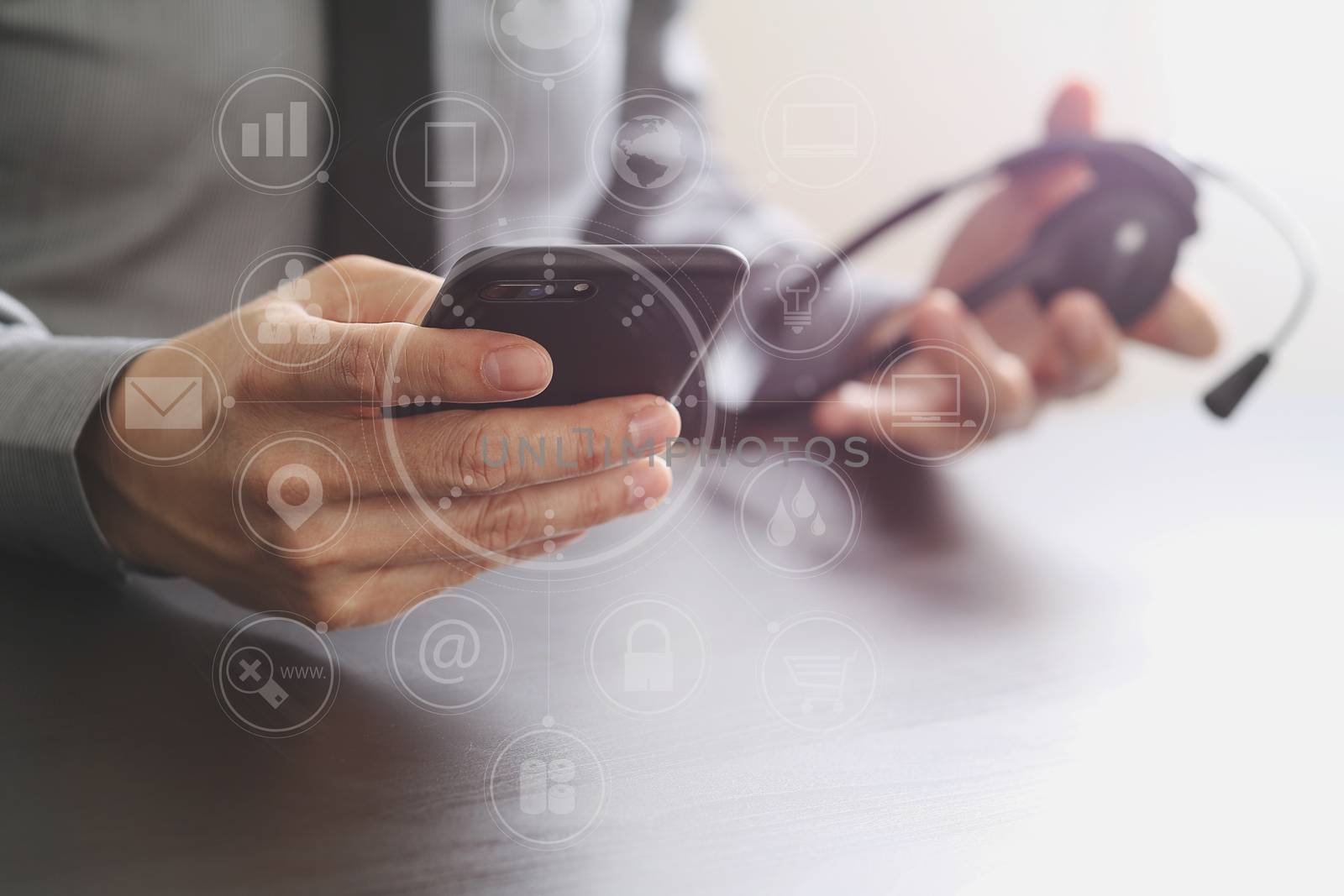 businessman using VOIP headset with mobile phone and concept communication call center on wooden desk with virtual reality icon diagram