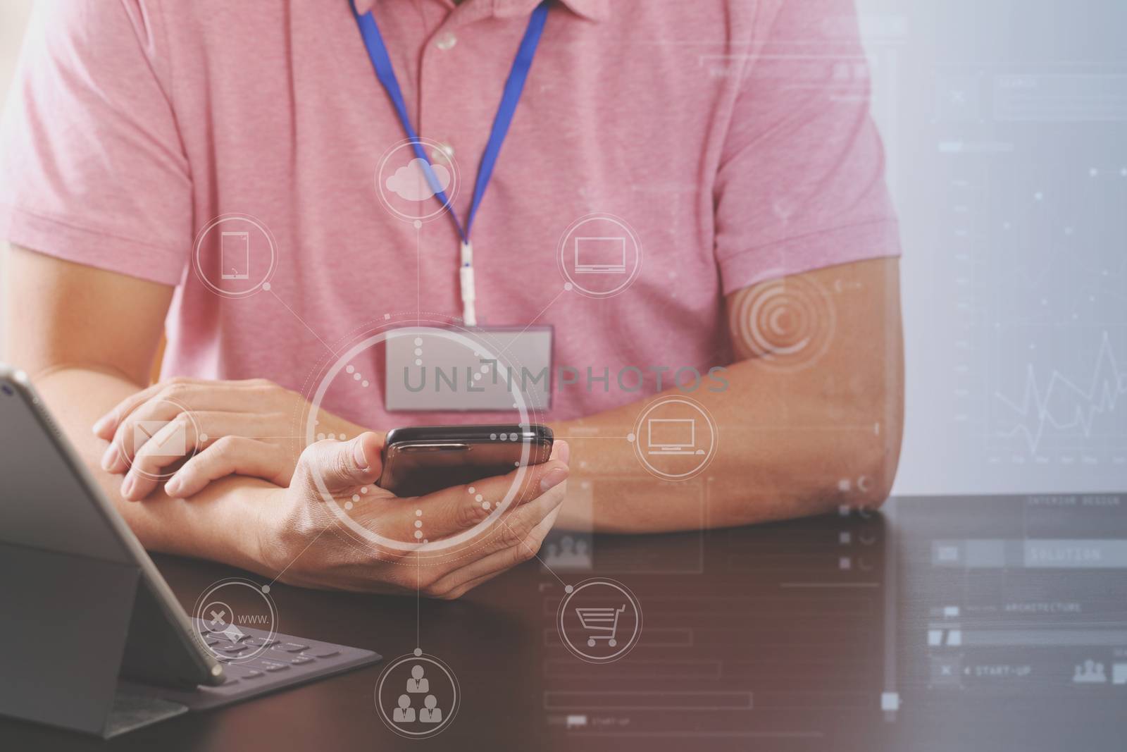 businessman in pink t-shirt working with smart phone and digitl tablet computer on wooden desk in modern office with virtual icon diagram