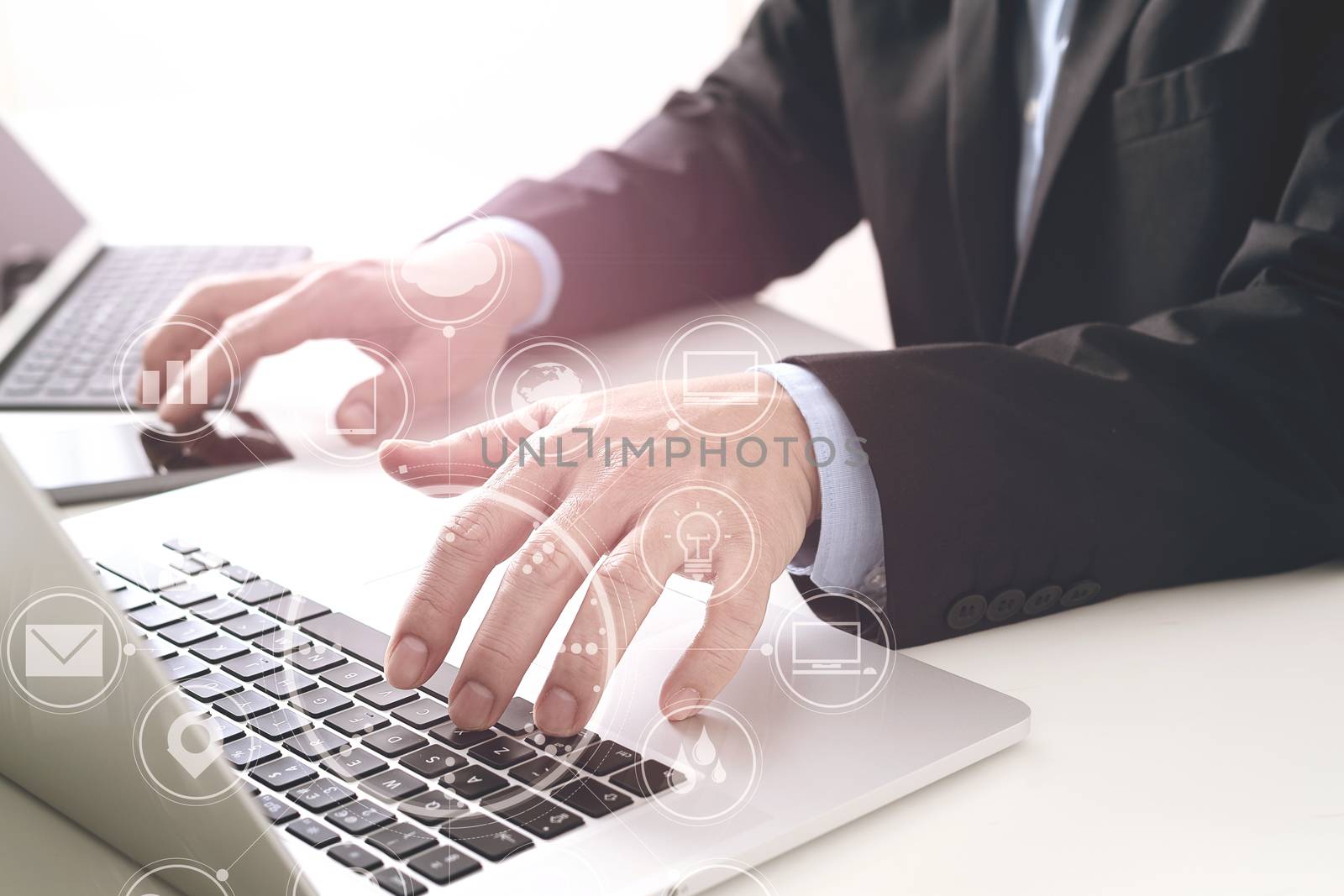 Hands of businessman typing on laptop in modern office with smart phone and digital tablet computer with VR icon diagram