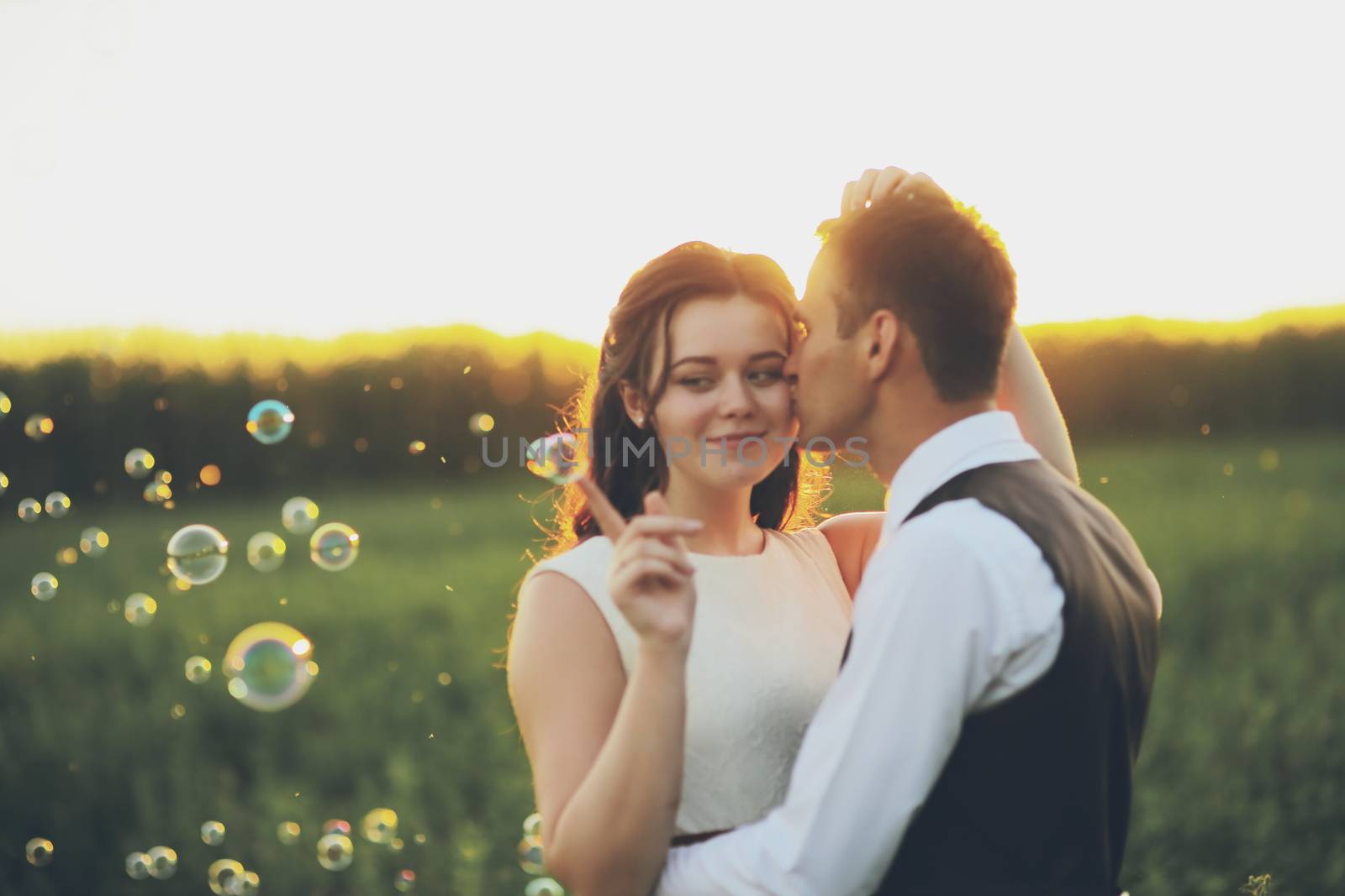 Happy bride and groom hug each other in the park at sunset. Soap bubbles. Wedding. Happy love concept. by selinsmo