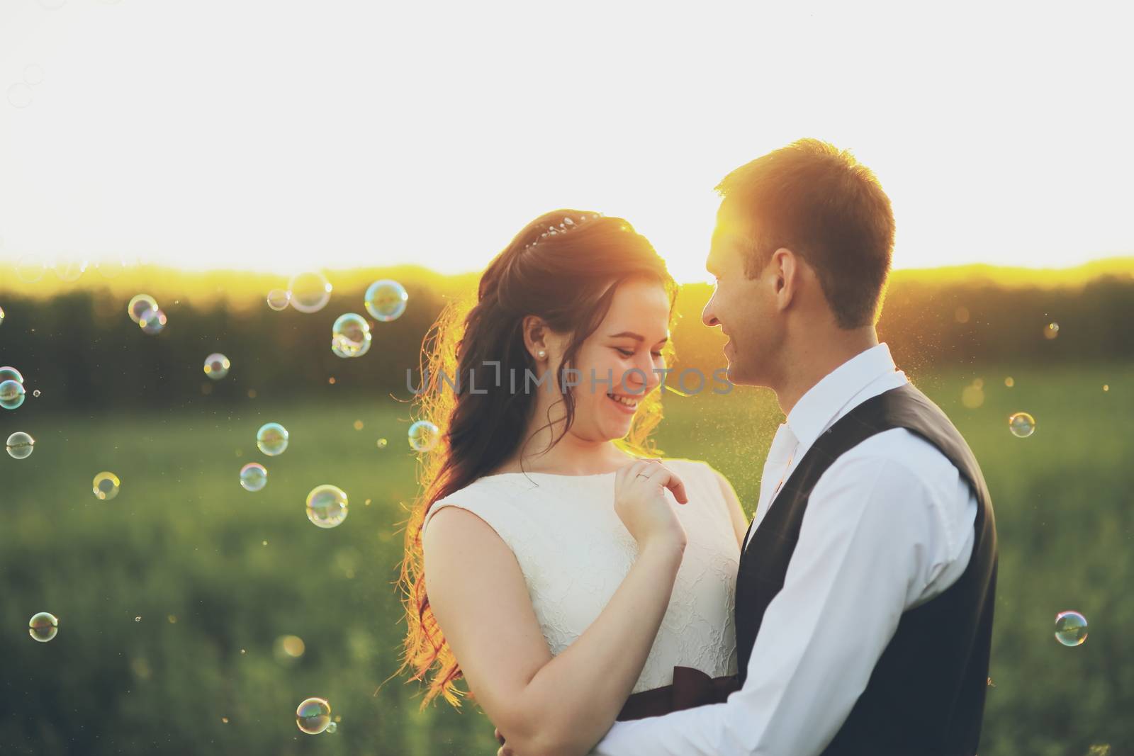 Happy bride and groom hug each other in the park at sunset. Soap bubbles. Wedding. Happy love concept. by selinsmo