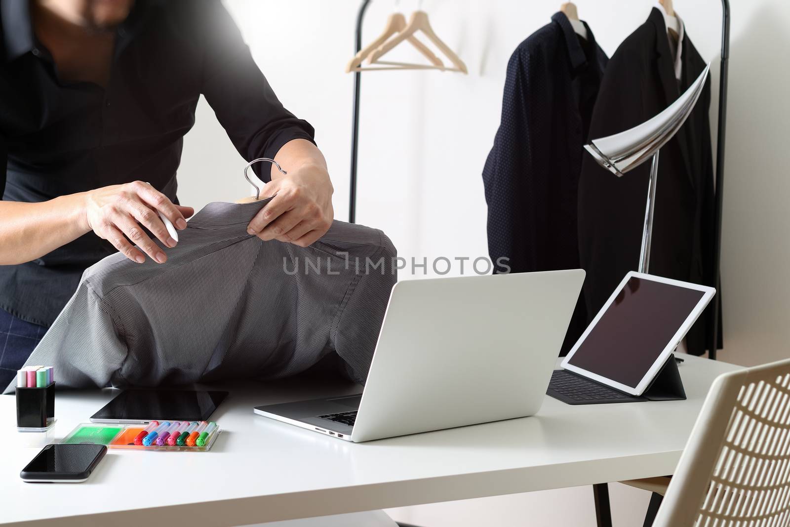 Fashion designer holding shirt and using laptop with digital tab by everythingpossible
