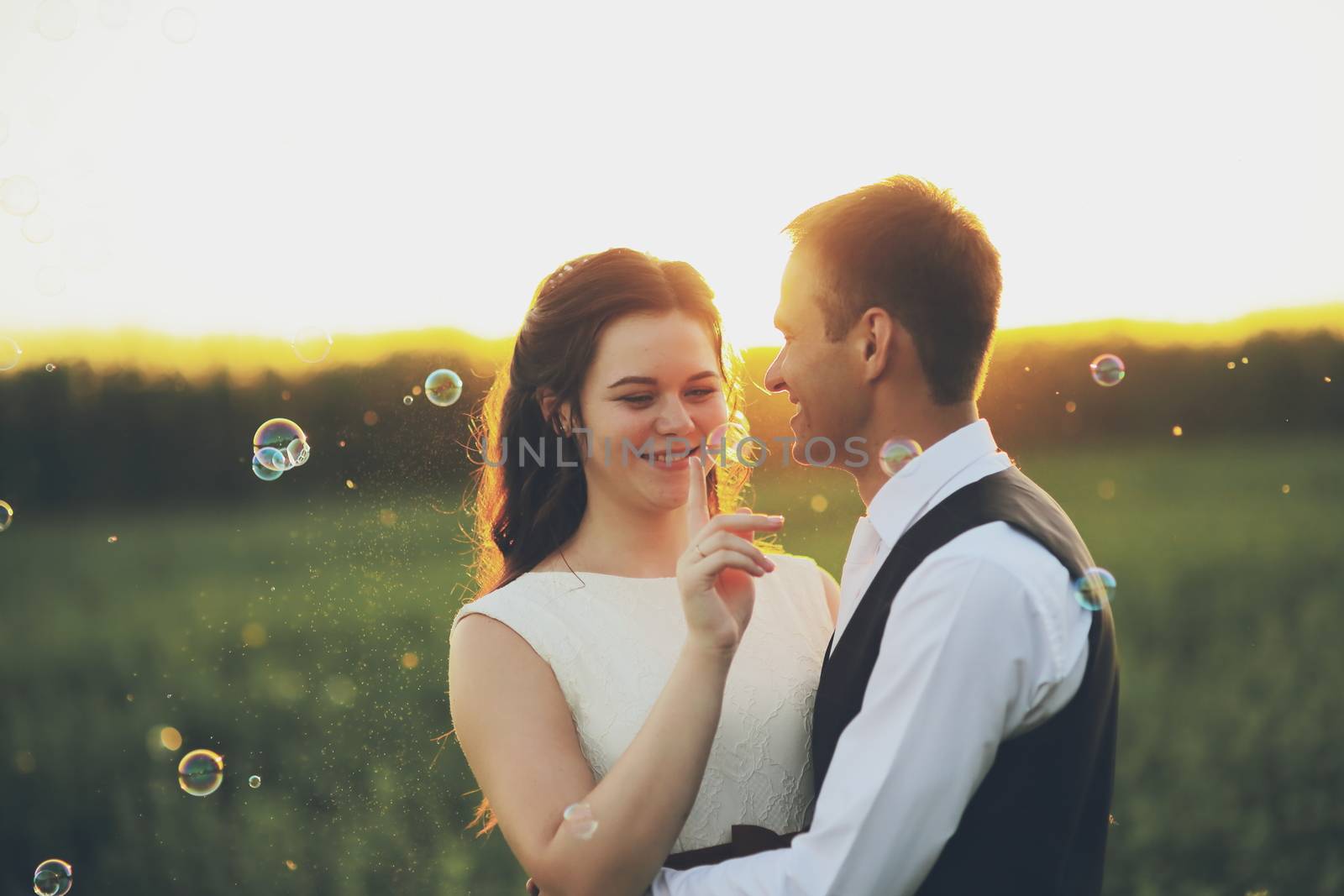 Happy bride and groom hug each other in the park at sunset. Soap bubbles. Wedding. Happy love concept. by selinsmo