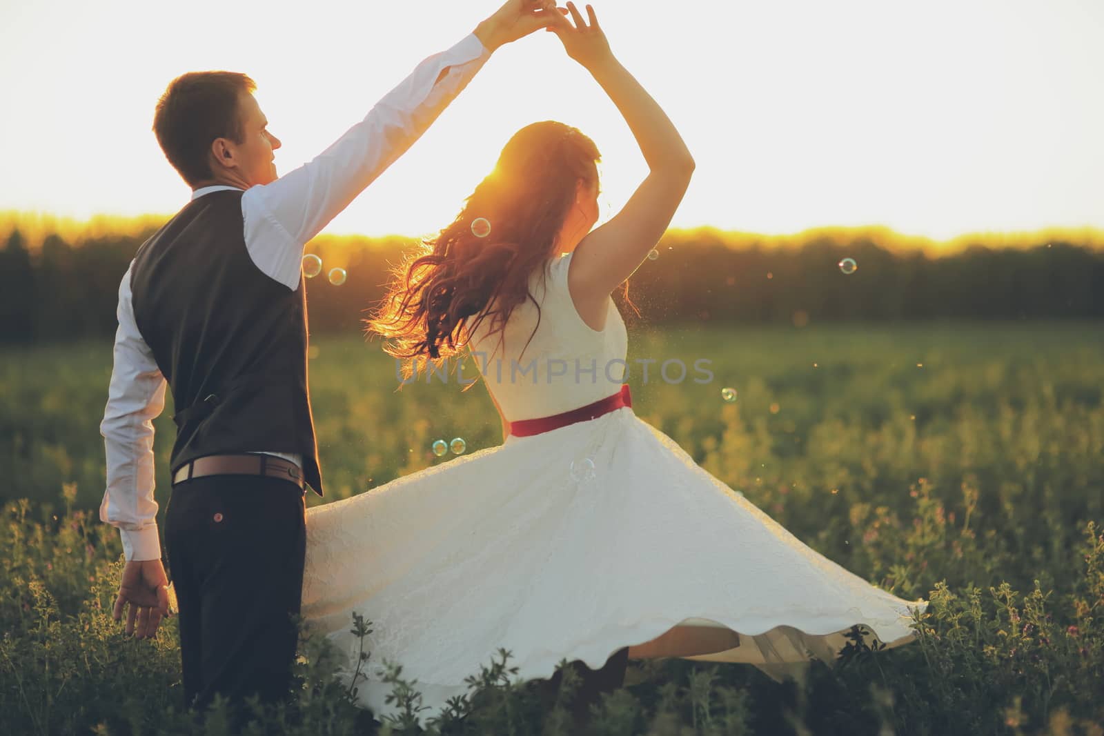 The bride and groom hold hands dancing in the park. Sunset light. Soap bubbles. Wedding. Happy family concept. High quality photo