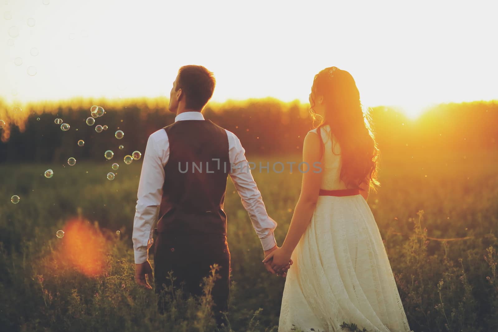The bride and groom hold hands and walk in the park. Sunset light. Bubble. Wedding. Happy family concept. by selinsmo