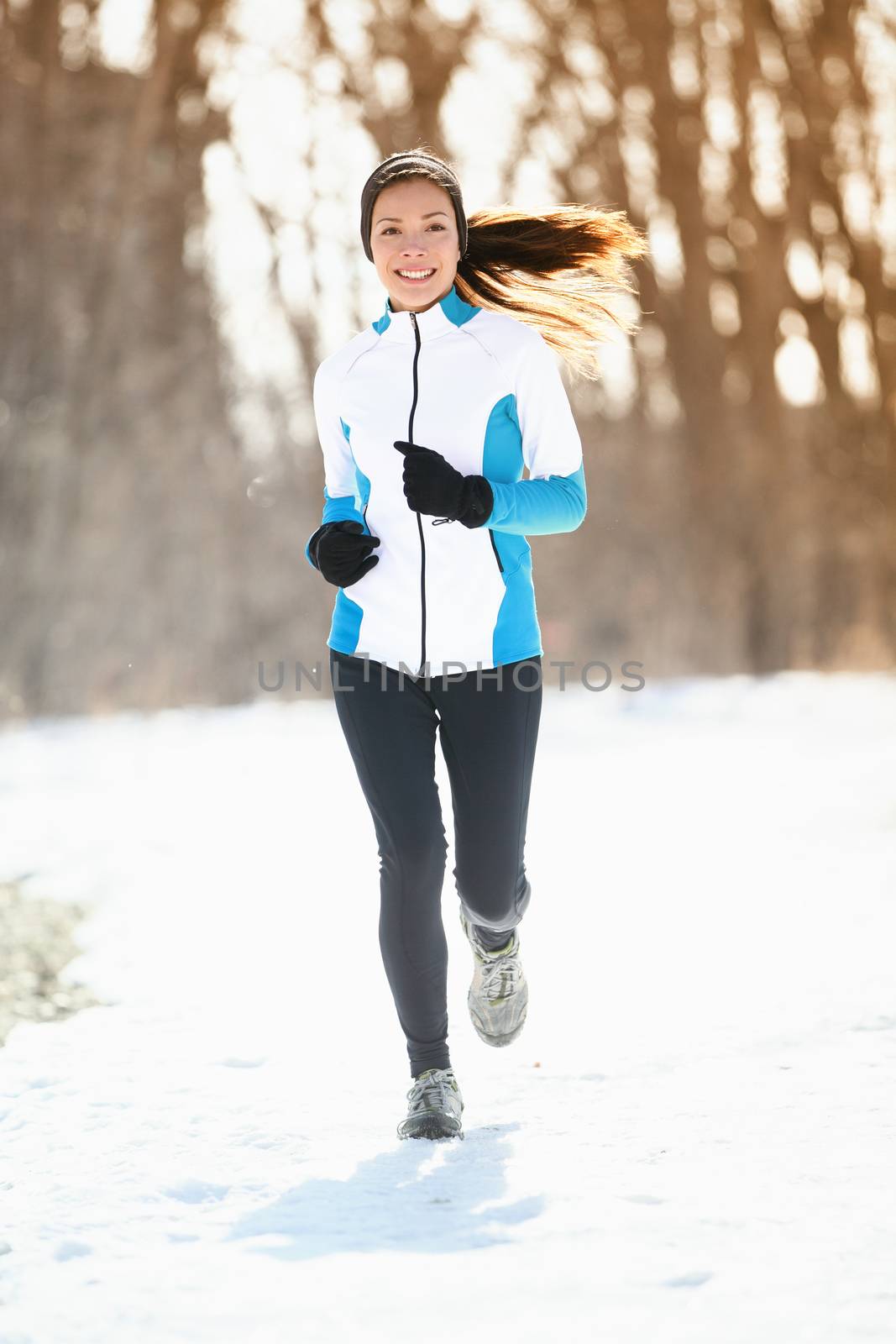 Winter running. Woman runner trail running cold winter forest landscape. Mixed race Asian / Caucasian female cross country running in warm clothes