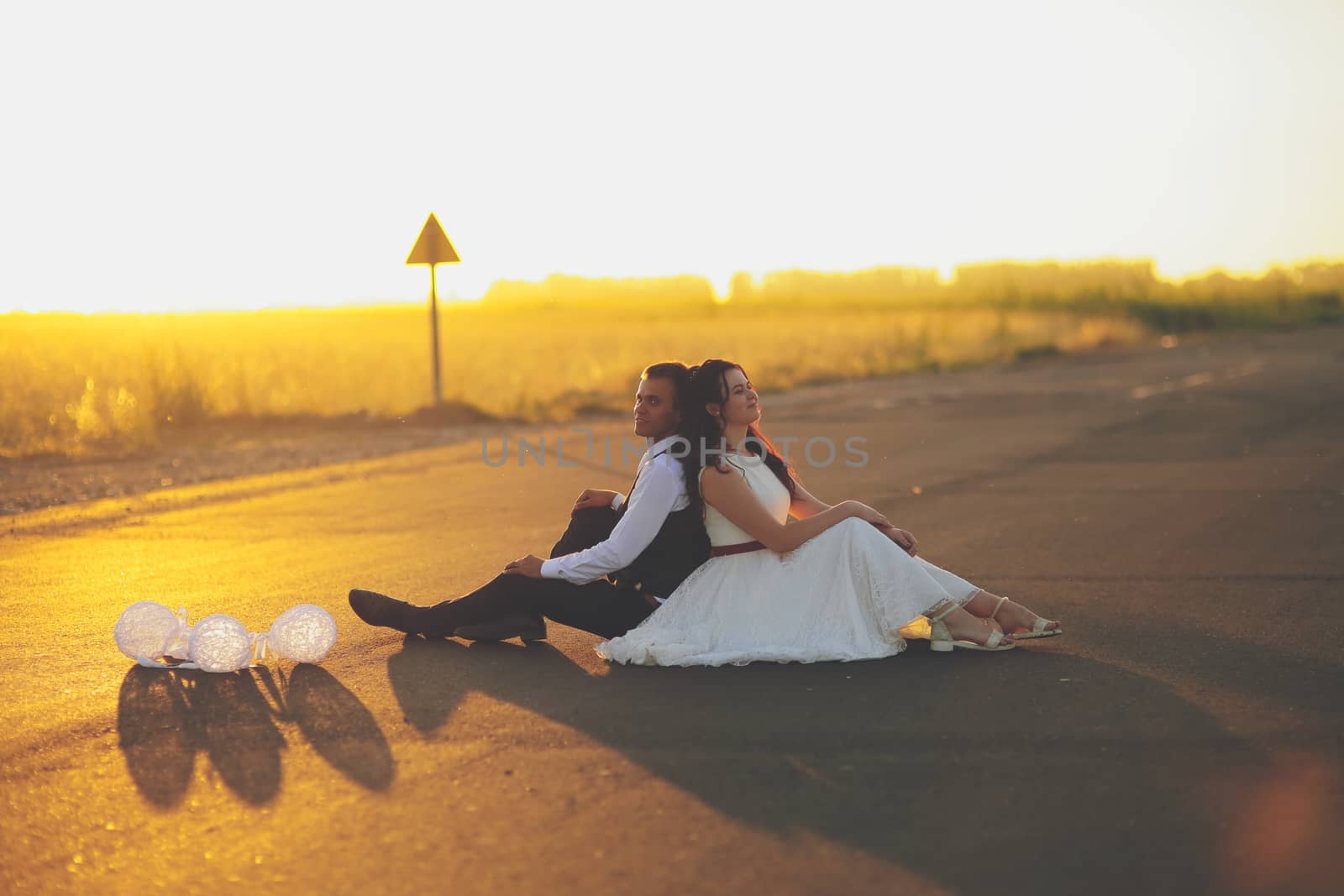 The bride and groom sit with their backs to each other in the sunset light. wedding. Happy love concept. by selinsmo