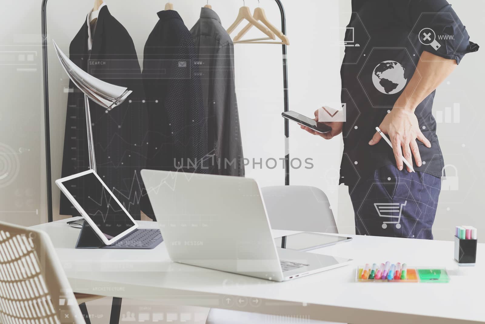 Fashion designer talking mobile phone and using laptop with digital tablet computer in modern studio with VR icon diagram