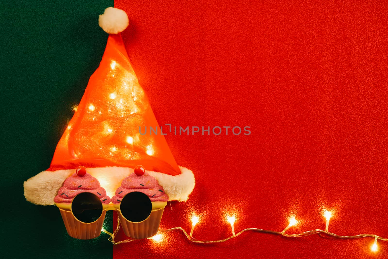 Greeting Season concept.Santa Claus hat with star light and glasses that decoration with Christmas cupcake on red and green background