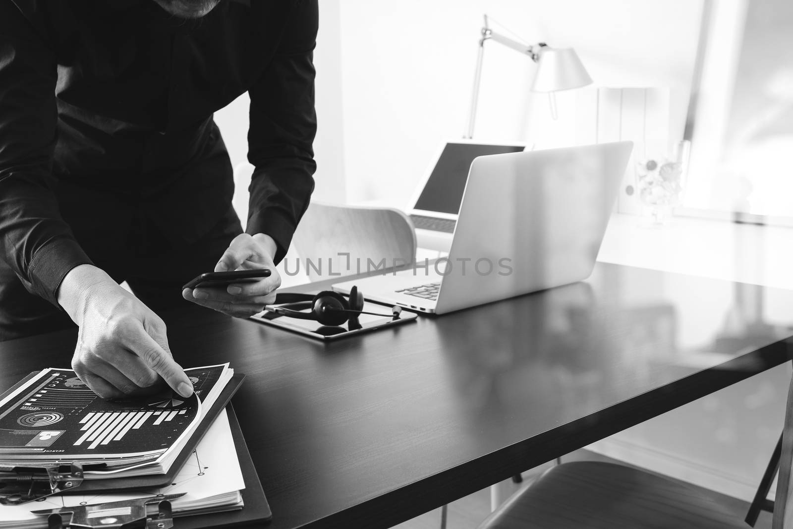 businessman or Designer using smart phone with latop and digital tablet computer and document on desk in modern office,black and white