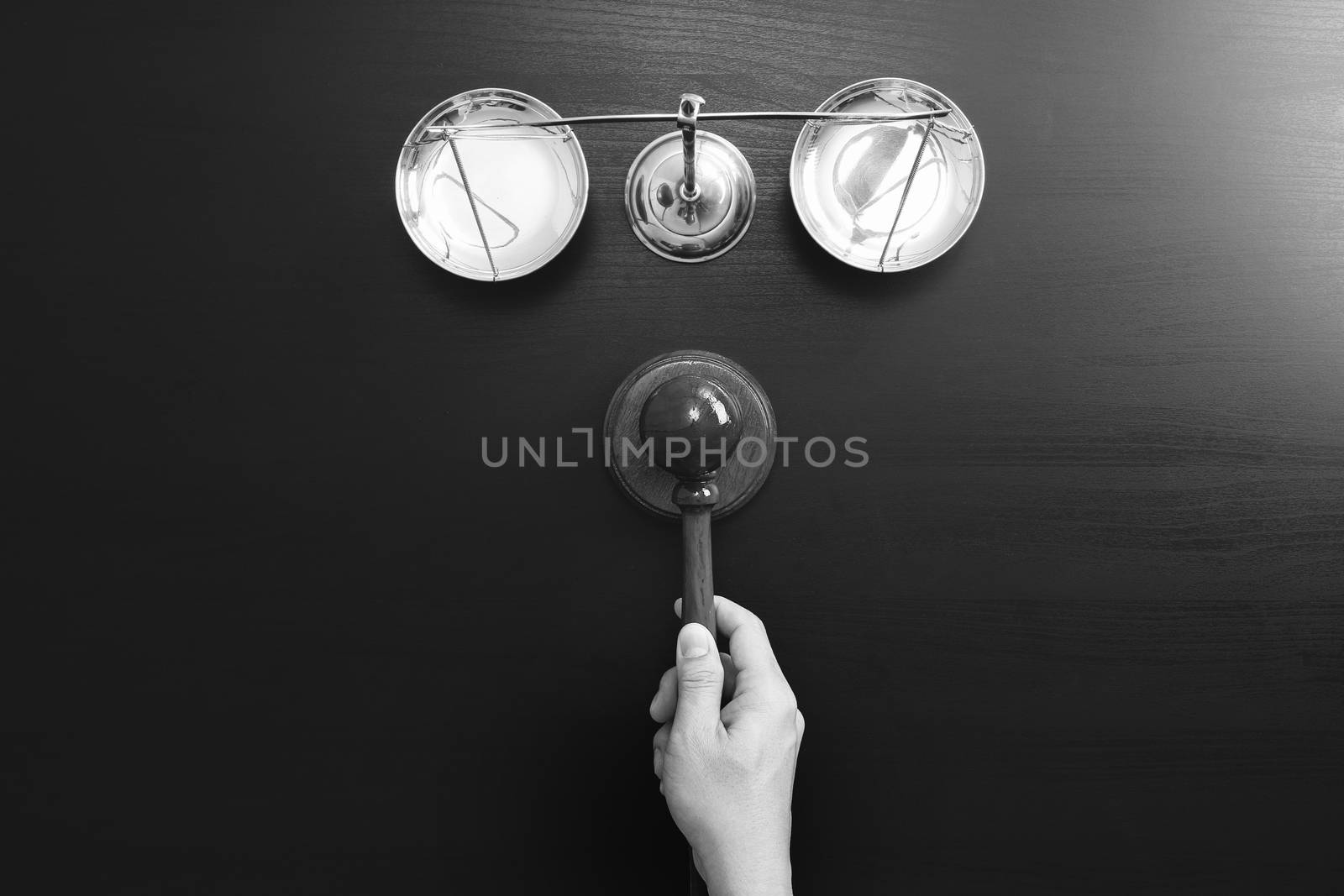 justice and law concept.Top view of Male judge hand in a courtroom with the gavel and brass scale on dark wood table,black and white 