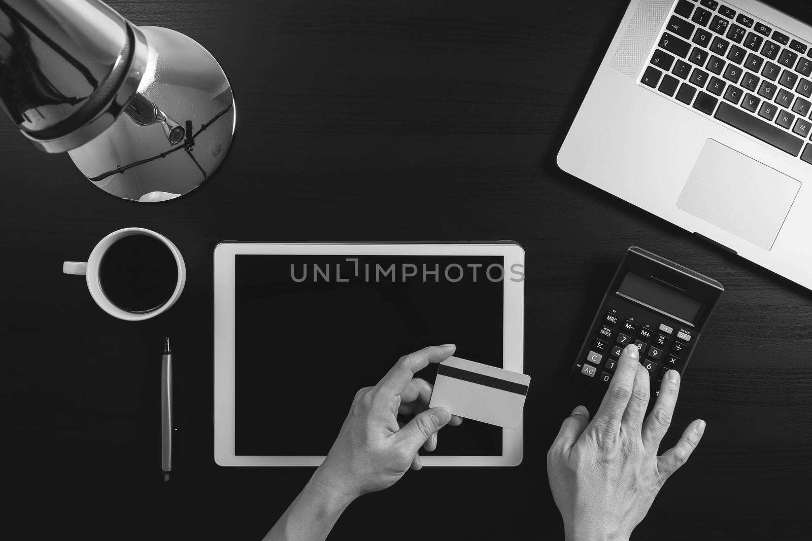 Internet shopping concept.Top view of hands working with laptop and credit card and tablet computer on dark wooden table background,black and white