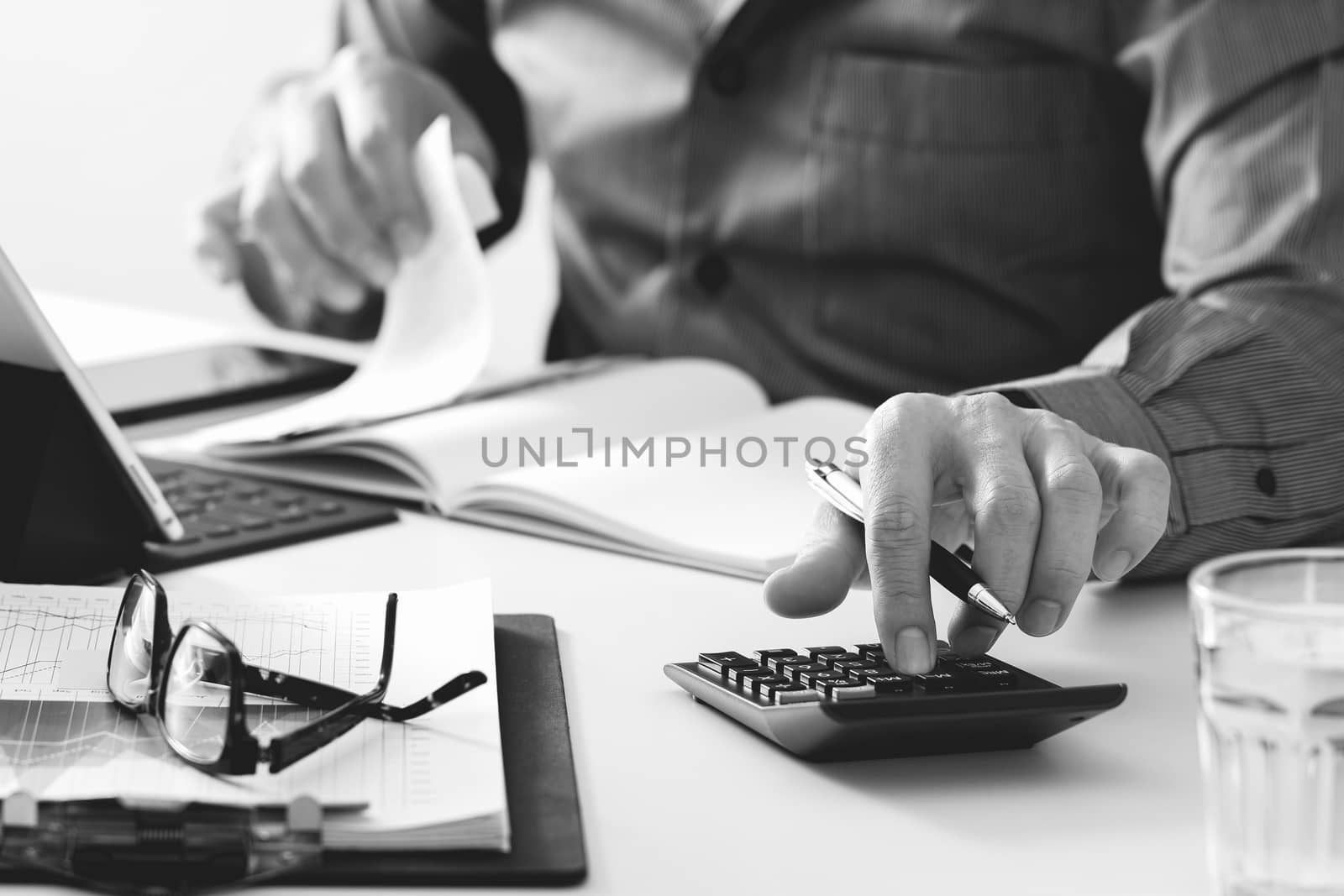 businessman hand working with finances about cost and calculator and latop with mobile phone on withe desk in modern office,black and white