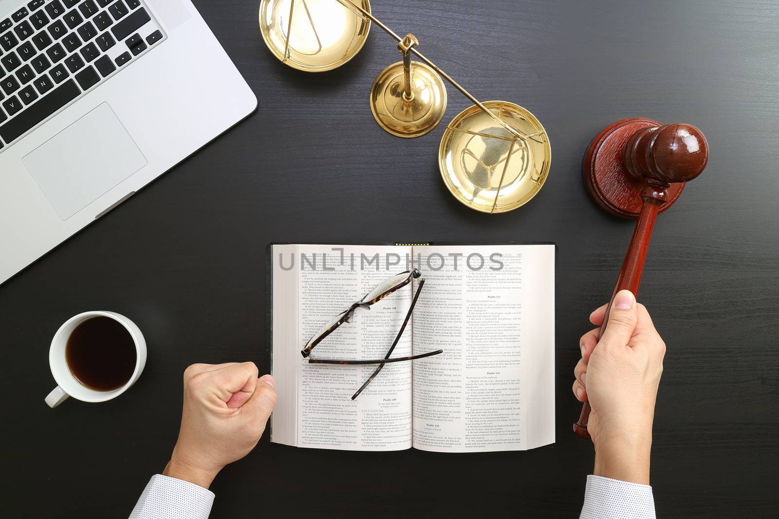 justice and law concept.Top view of Male judge hand in a courtroom with the gavel and brass scale and computer and open bible book on dark wood table