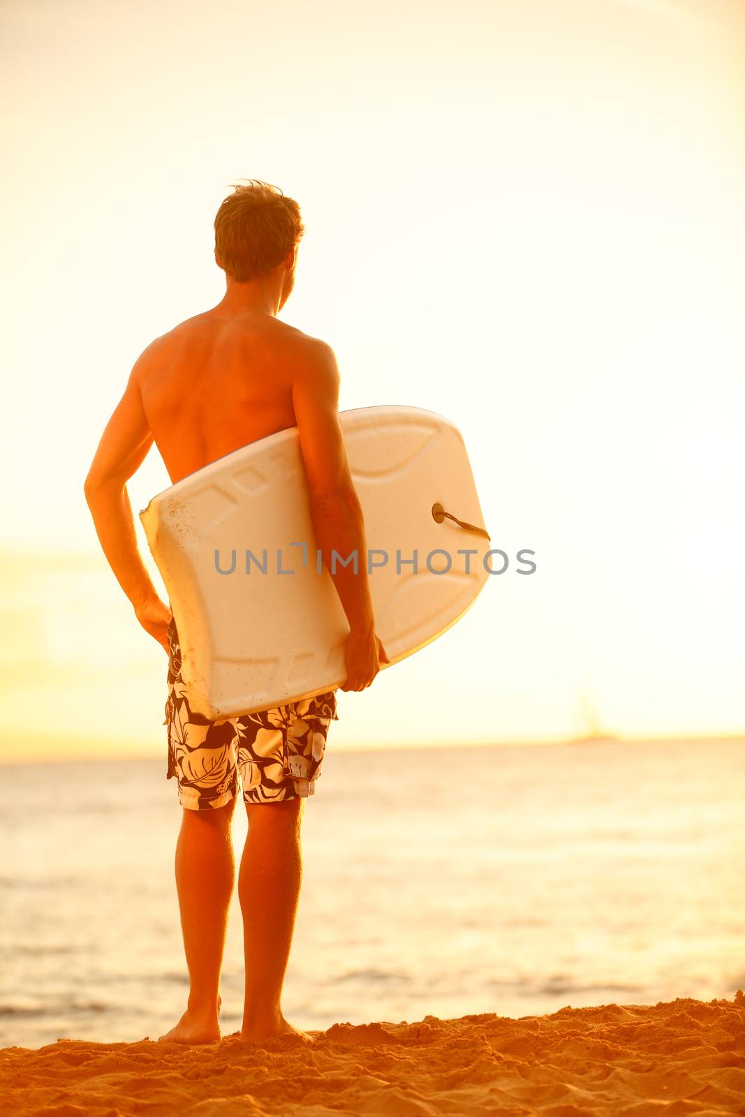 Surfer man on beach at surfing sunset holding bodyboard. Fit male body surfer guy enjoying sunset and bodyboarding on summer holidays vacation on tropical beach. Kaanapali beach, Maui, Hawaii.
