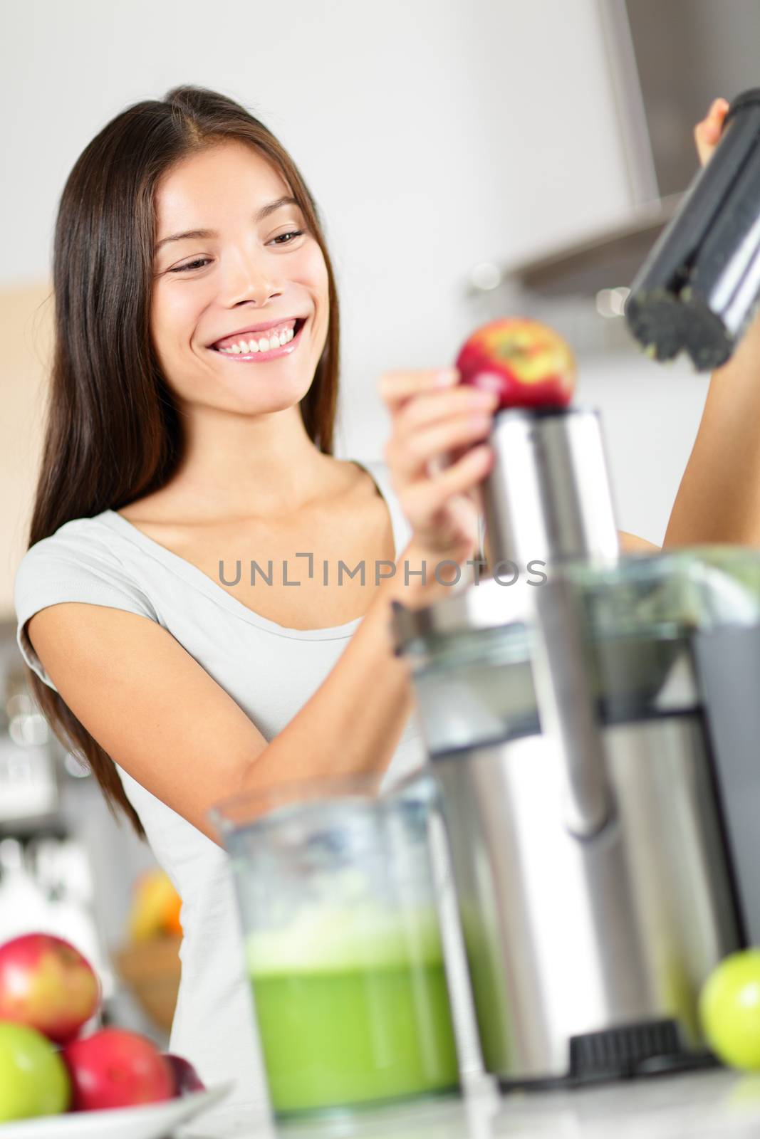 Woman making apple and vegetable juice on juicer machine at home in kitchen. Juicing and healthy eating happy woman making green vegetable and fruit juice. Mixed race Asian Caucasian model.