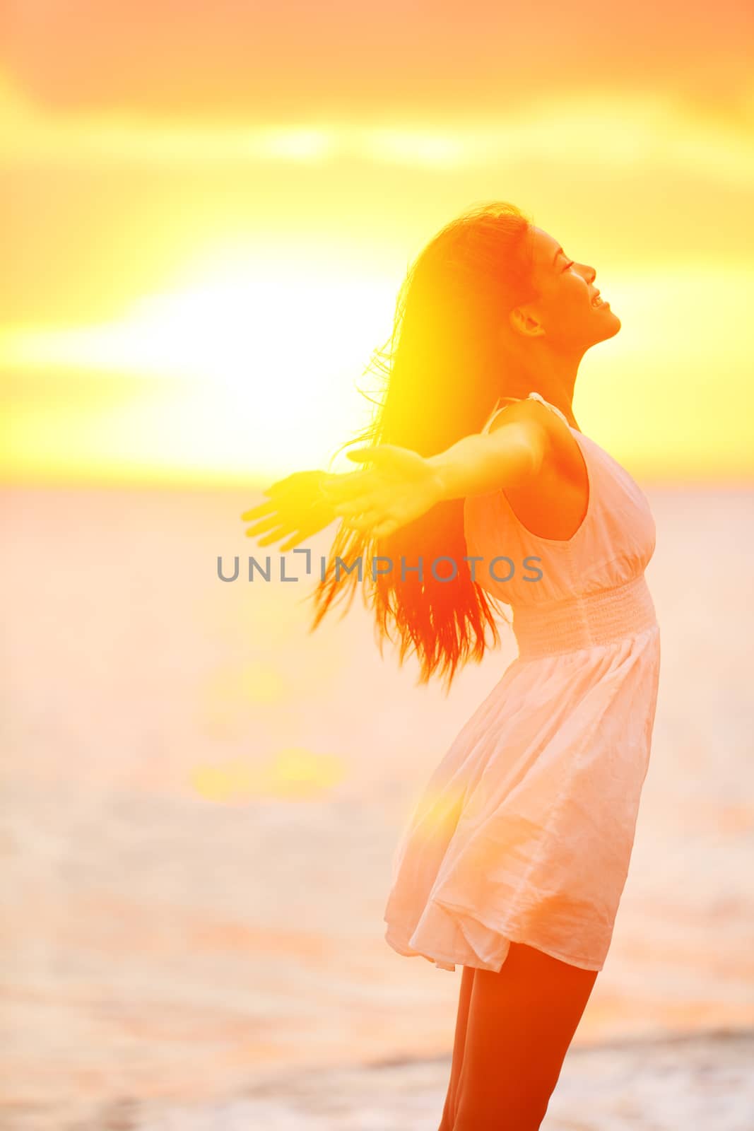 Freedom woman enjoying feeling happy free at beach at sunset. Beautiful serene relaxing woman in pure happiness and elated enjoyment with arms raised outstretched up. Asian Caucasian female model.