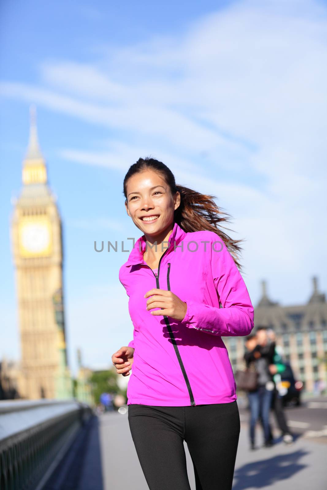 Running woman in London living healthy lifestyle. Female runner jogging near Big Ben in jacket. Urban fitness girl smiling happy working out on Westminster Bridge, London, England, United Kingdom.