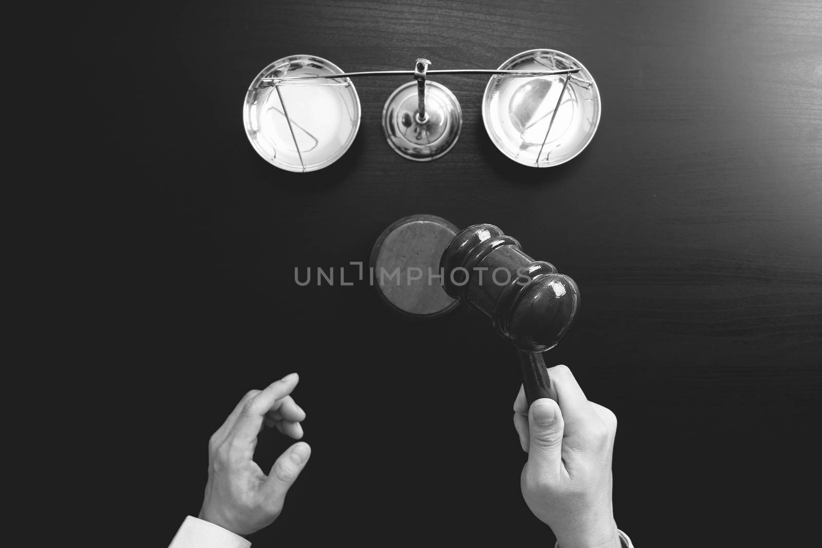 justice and law concept.Top view of Male judge hand in a courtroom with the gavel and brass scale on dark wood table,black and white