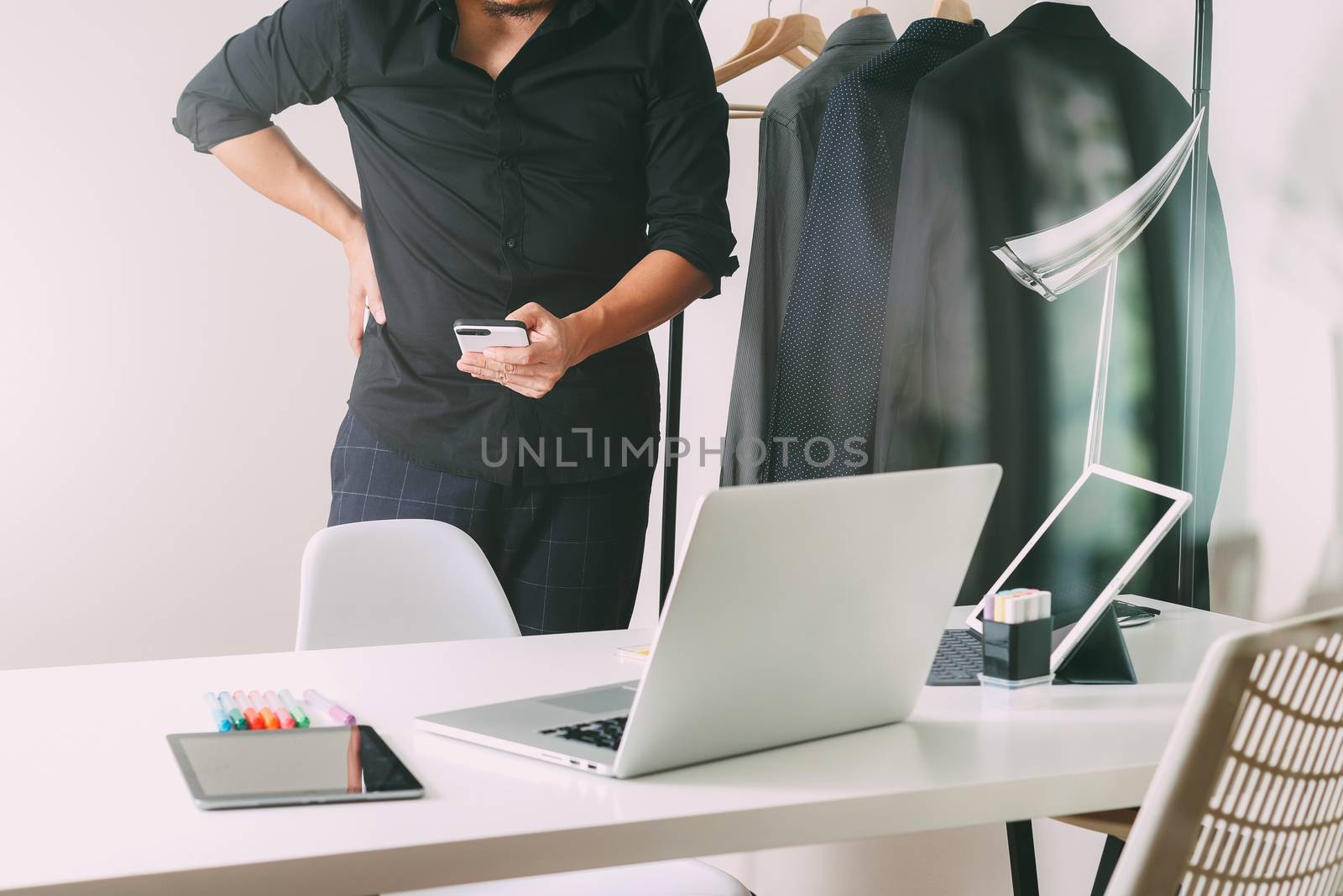 Fashion designer using mobile phone and using laptop with digital tablet computer in modern studio 