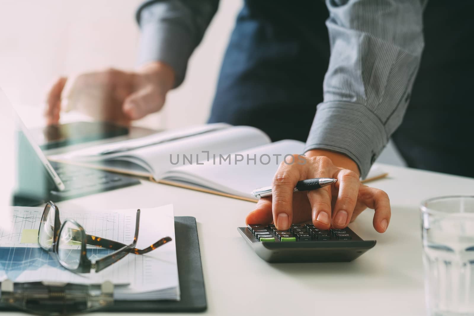 businessman hand working with finances about cost and calculator and latop with mobile phone on withe desk in modern office 
