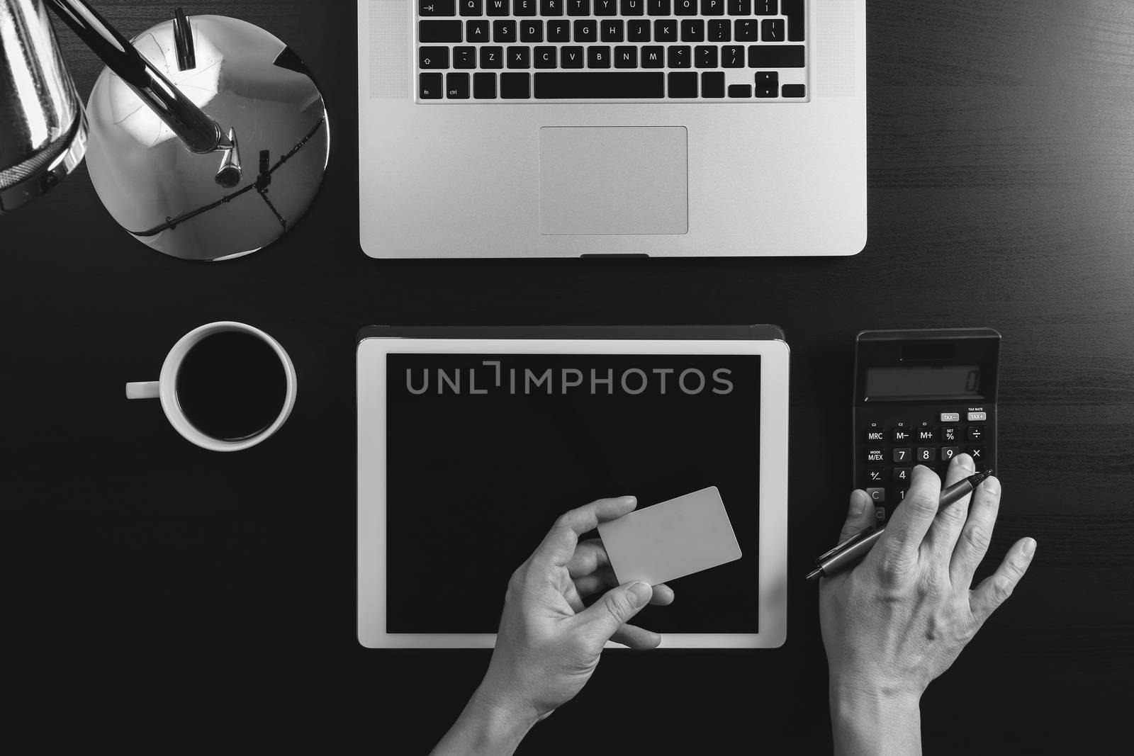 Internet shopping concept.Top view of hands working with calculator and laptop and credit card and tablet computer on dark wooden table background,black and white